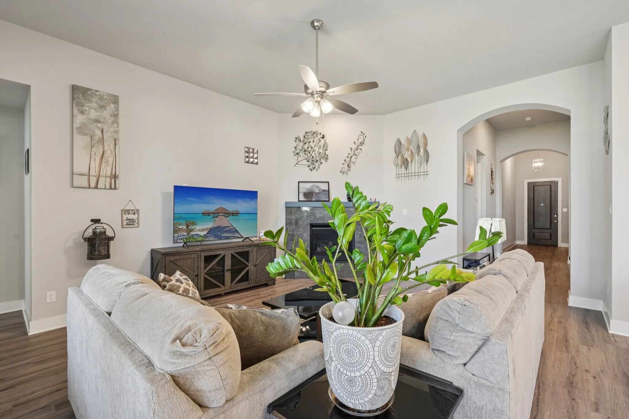 Spacious living area featuring wood-finish flooring, a ceiling fan with integrated lighting, a built-in fireplace with a stone-finish surround, and arched doorways