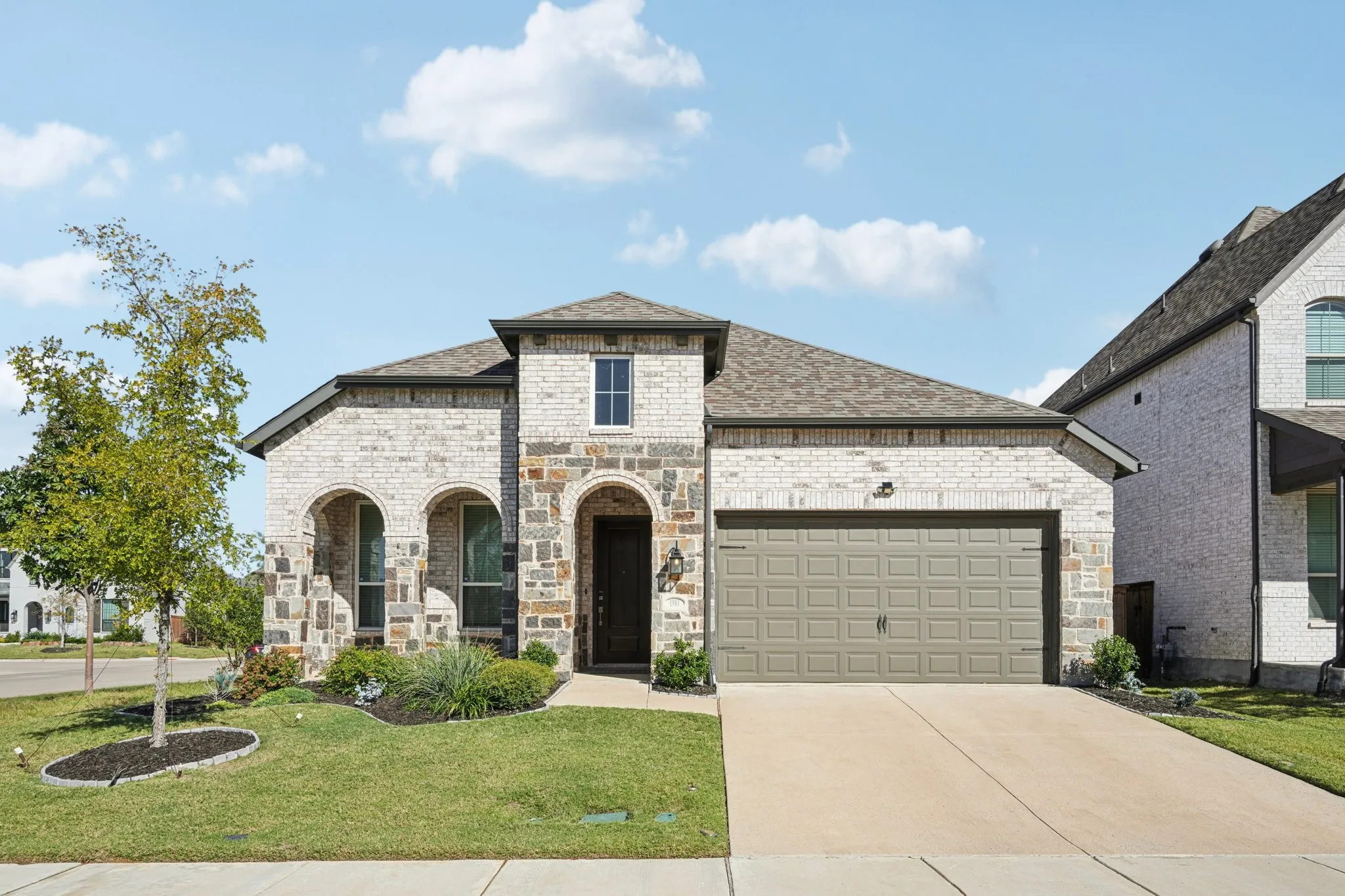 Exterior featuring light-colored brick, stone accents, arched entryways, an attached garage, and a landscaped lawn