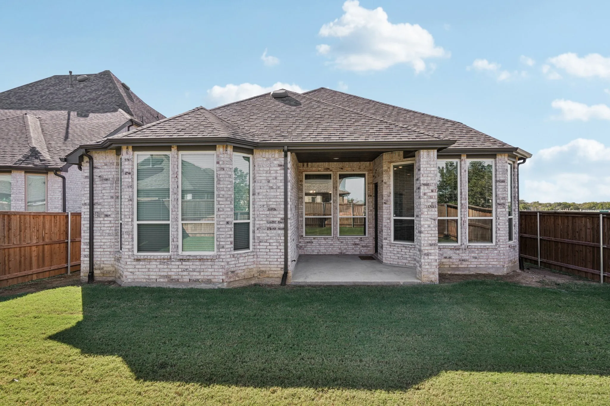 Expansive backyard featuring a manicured lawn, a covered patio, and a light brick exterior with multiple windows