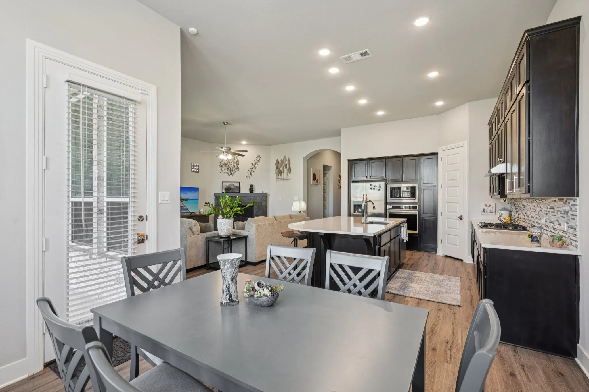Open-concept kitchen with dark wood-finish cabinetry, a central island with countertop seating, stainless steel appliances, and a mosaic tile backsplash