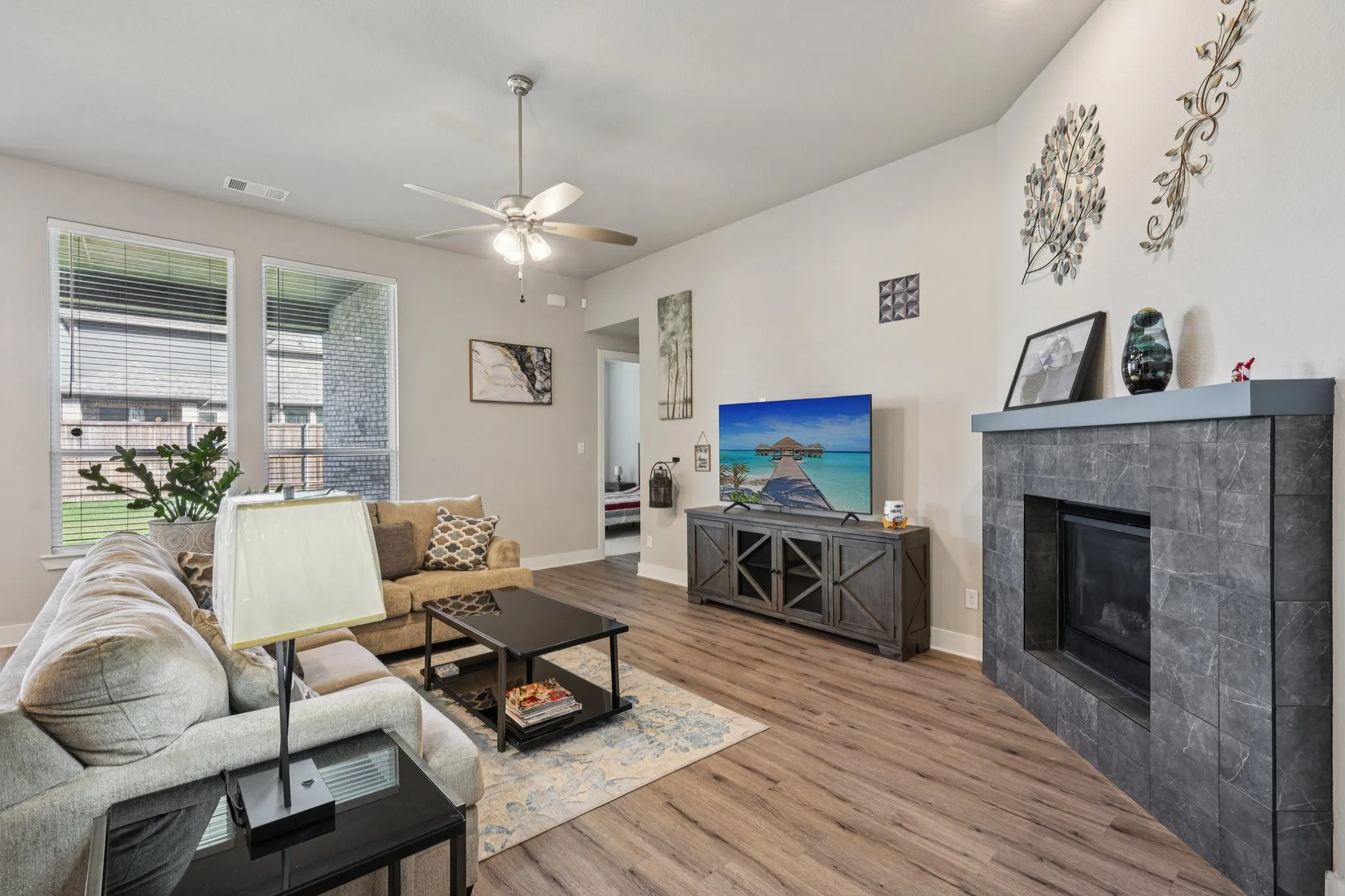 Living area with wood-finish flooring, a ceiling fan, and multiple windows