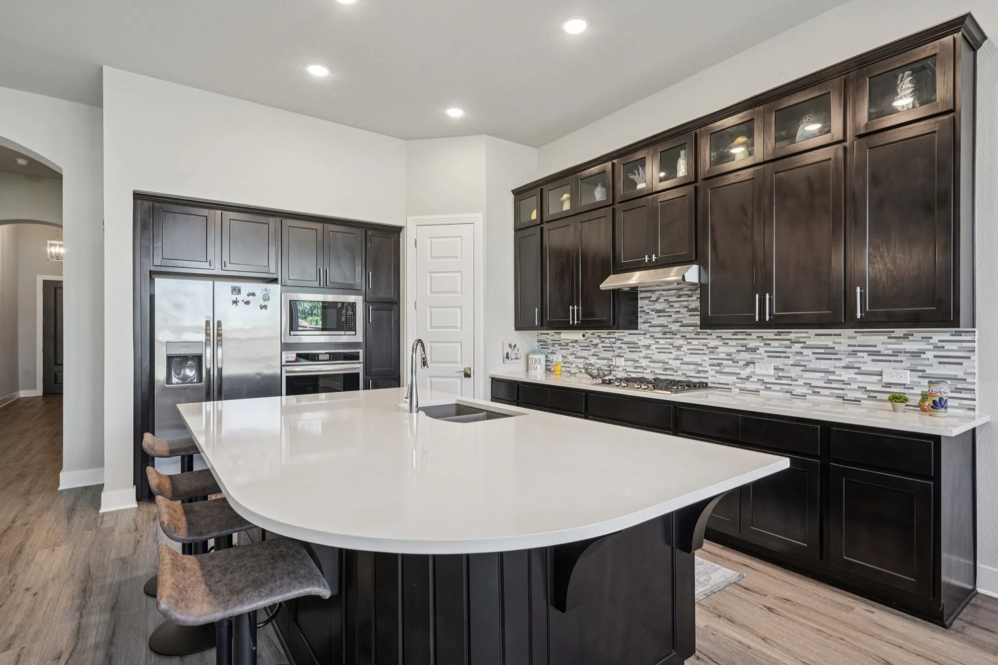Spacious kitchen featuring dark wood cabinetry, stainless steel appliances, a large central island with a white countertop, and wood-finish flooring