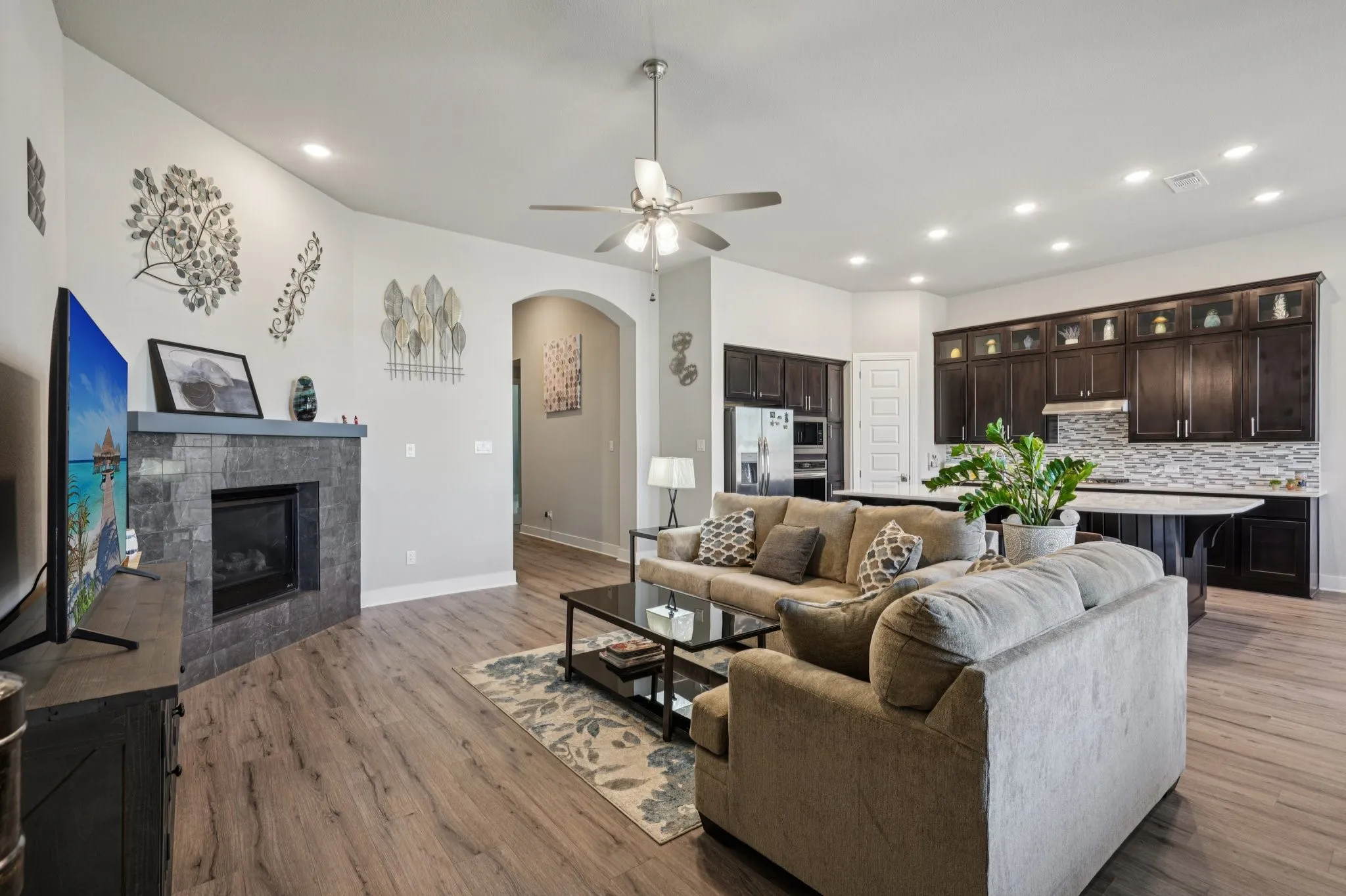 Open-concept living space featuring wood-finish flooring, a tiled fireplace with mantel, recessed lighting, and a ceiling fan