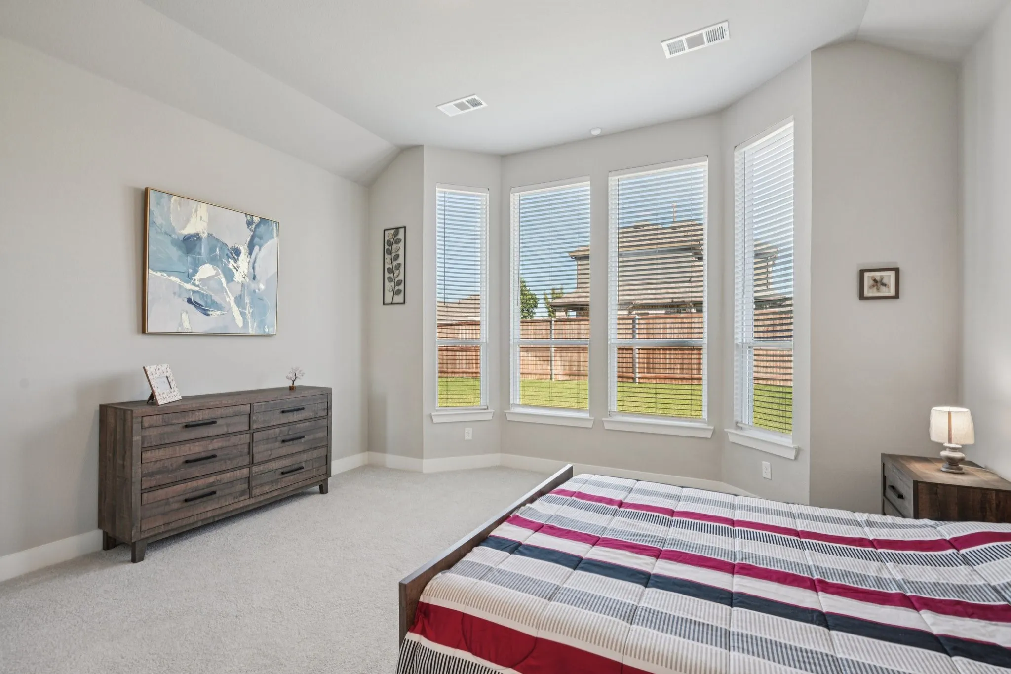 Vaulted ceiling, bay windows with blinds, light-toned carpeting, and neutral wall tones