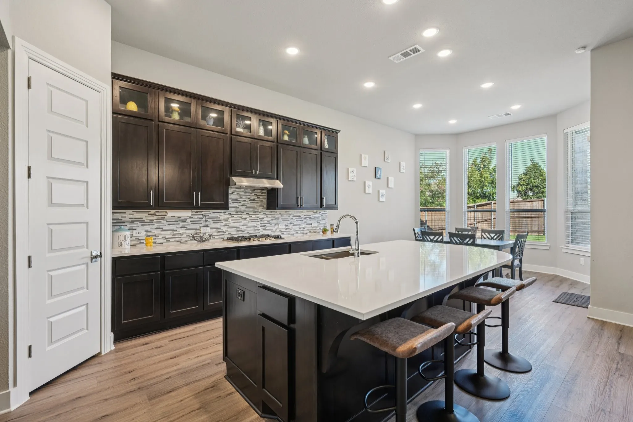 Kitchen featuring dark wood cabinetry, a large center island with a light-colored countertop, wood-finish flooring, and a patterned tile backsplash