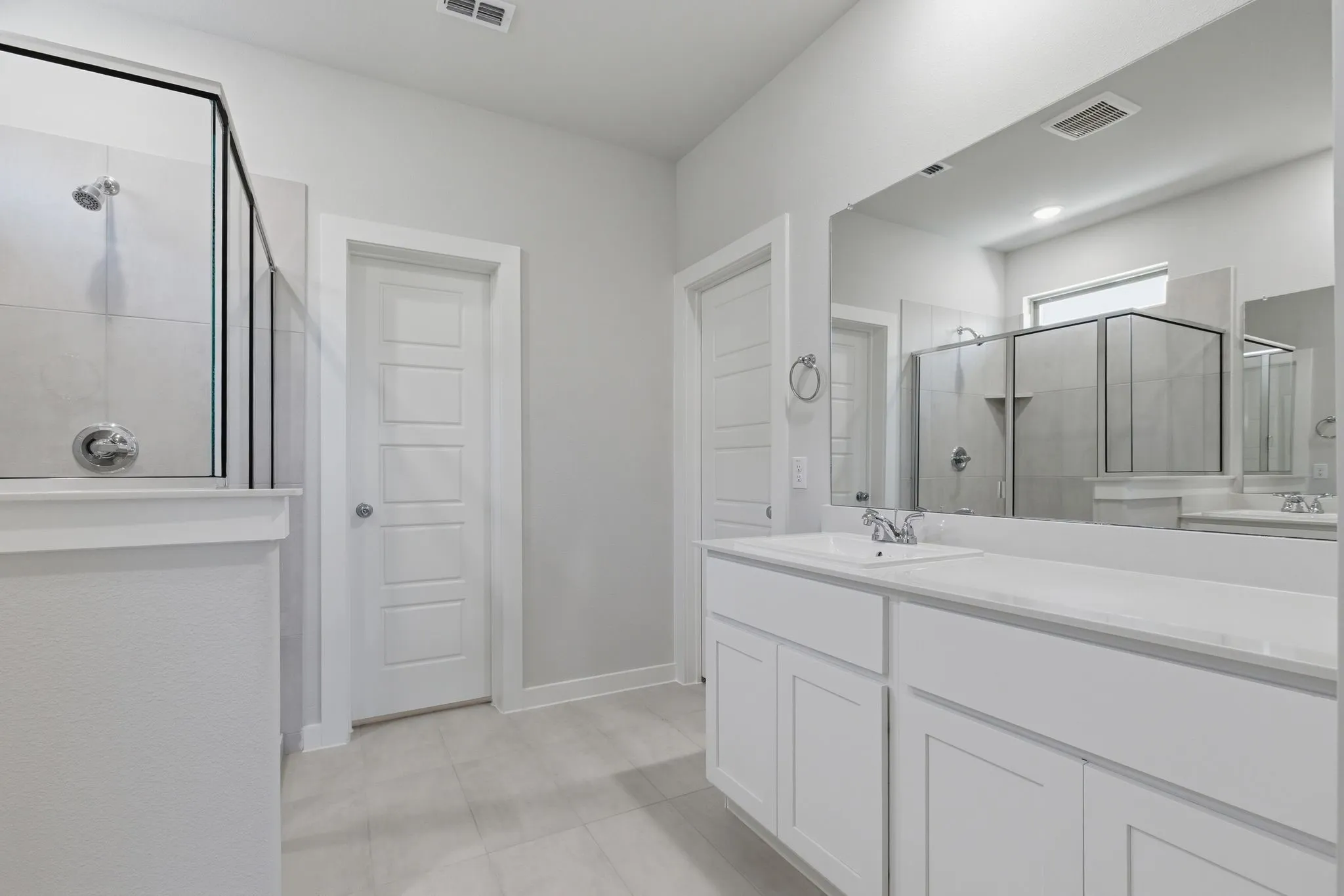 Spacious bathroom featuring a glass-enclosed shower, dual vanity with undermount sinks, stone countertops, and tile flooring