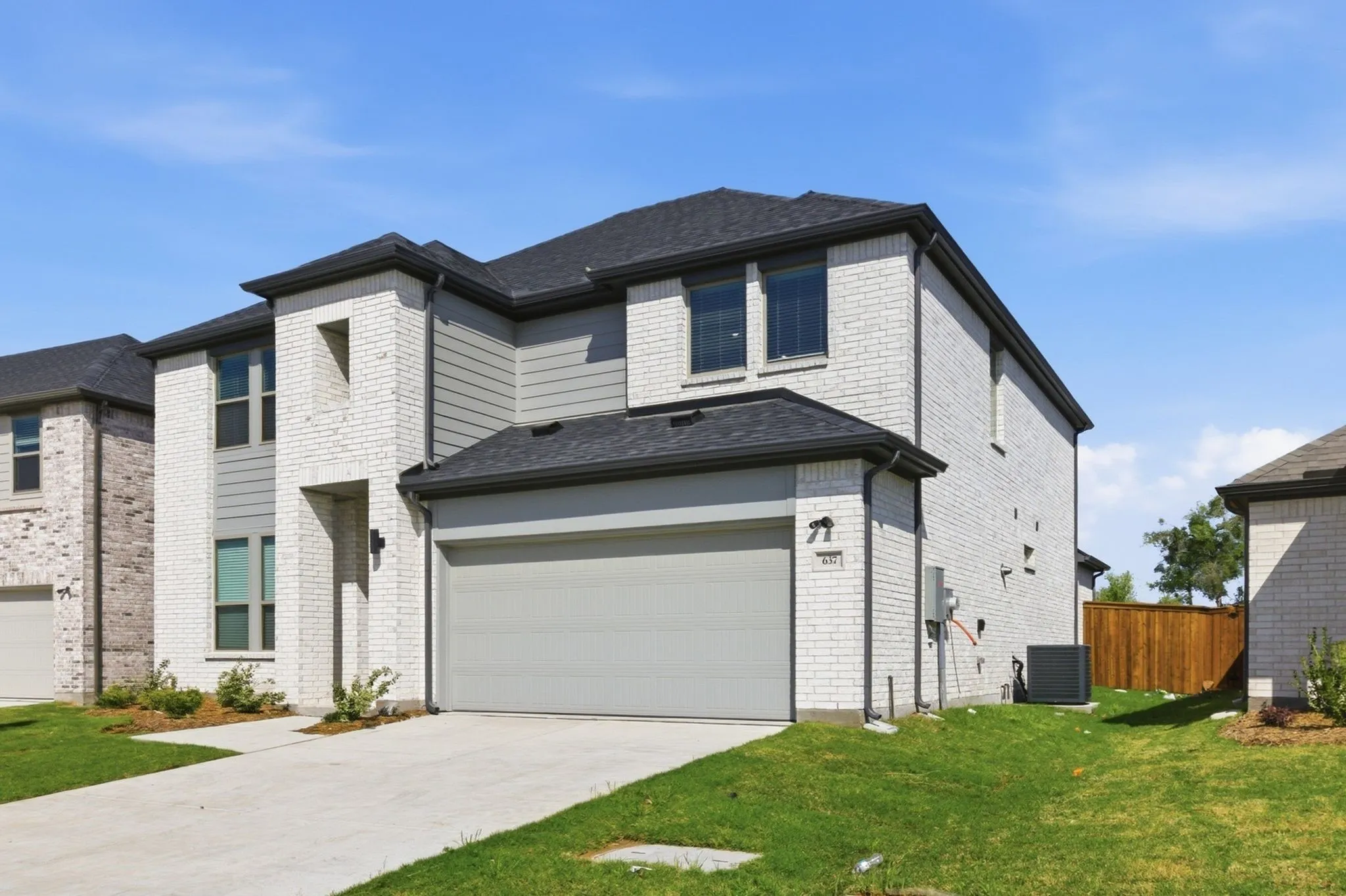 Two-story exterior featuring white brick and horizontal siding accents, a dark shingle roof, an attached two-car garage, and a concrete driveway