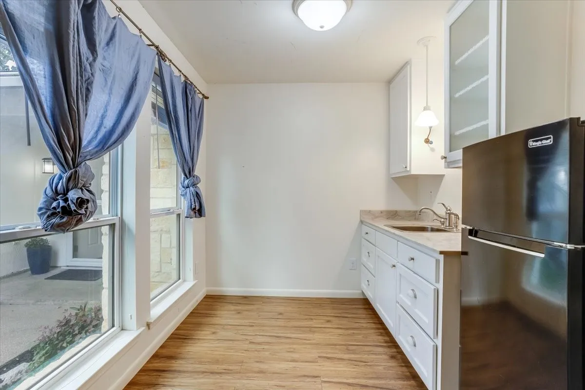 Wood-finish flooring, white cabinetry, integrated sink, and a compact refrigerator