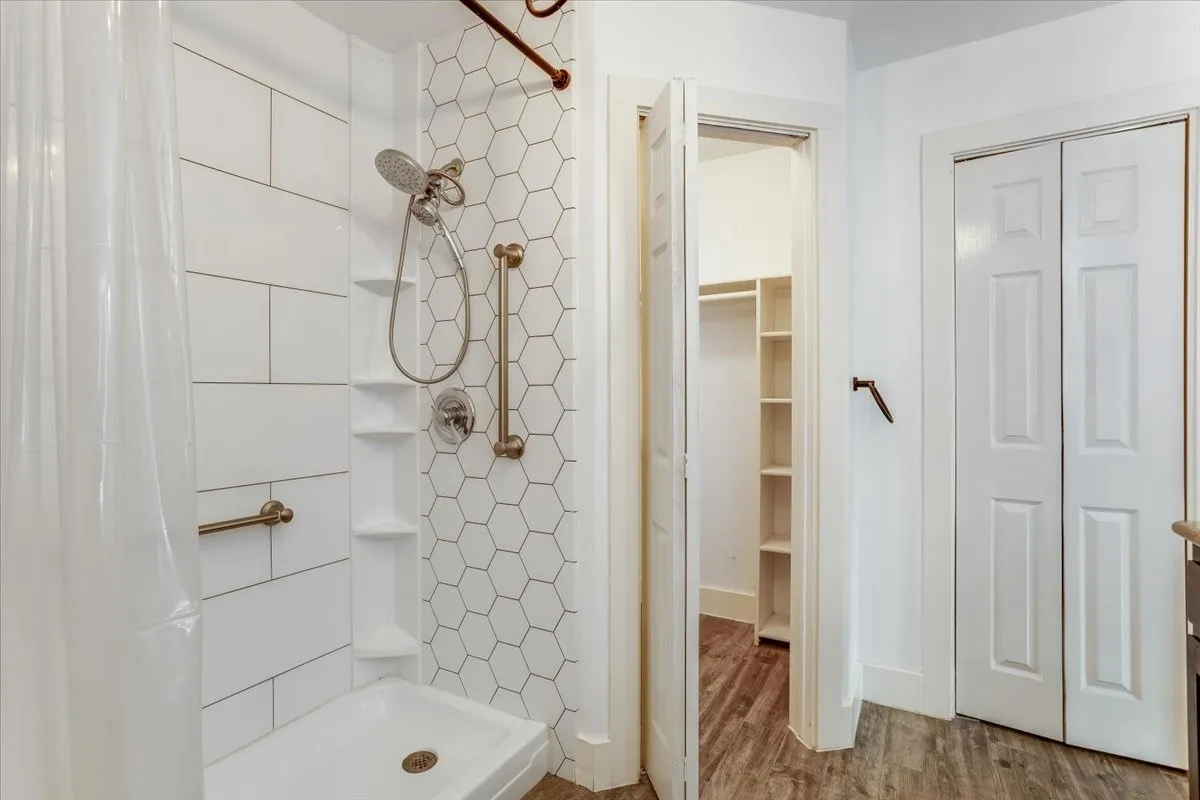 Shower featuring white subway tile surround, hexagonal accent tile, and bronze-finish grab bars