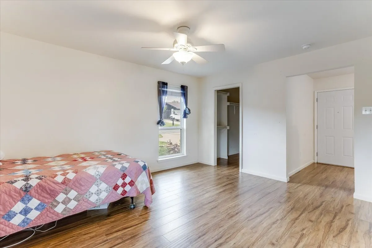 Wood-finish flooring, white walls, and a ceiling fan with integrated lighting