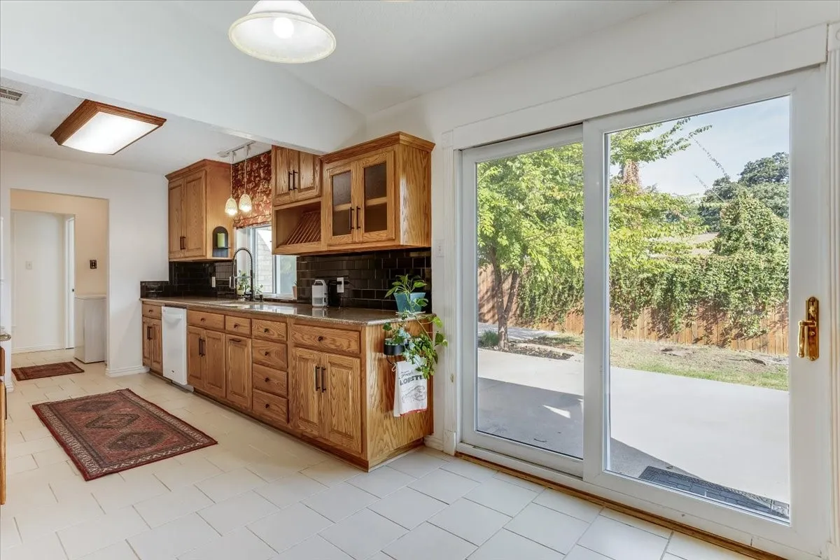 Kitchen featuring wood cabinetry, dark countertops, dark tile backsplash, and light tile flooring