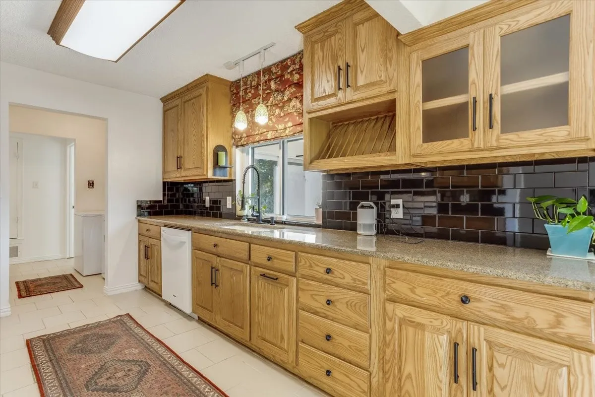 Light wood-finish cabinetry with black hardware, black subway tile backsplash, and light-toned countertops