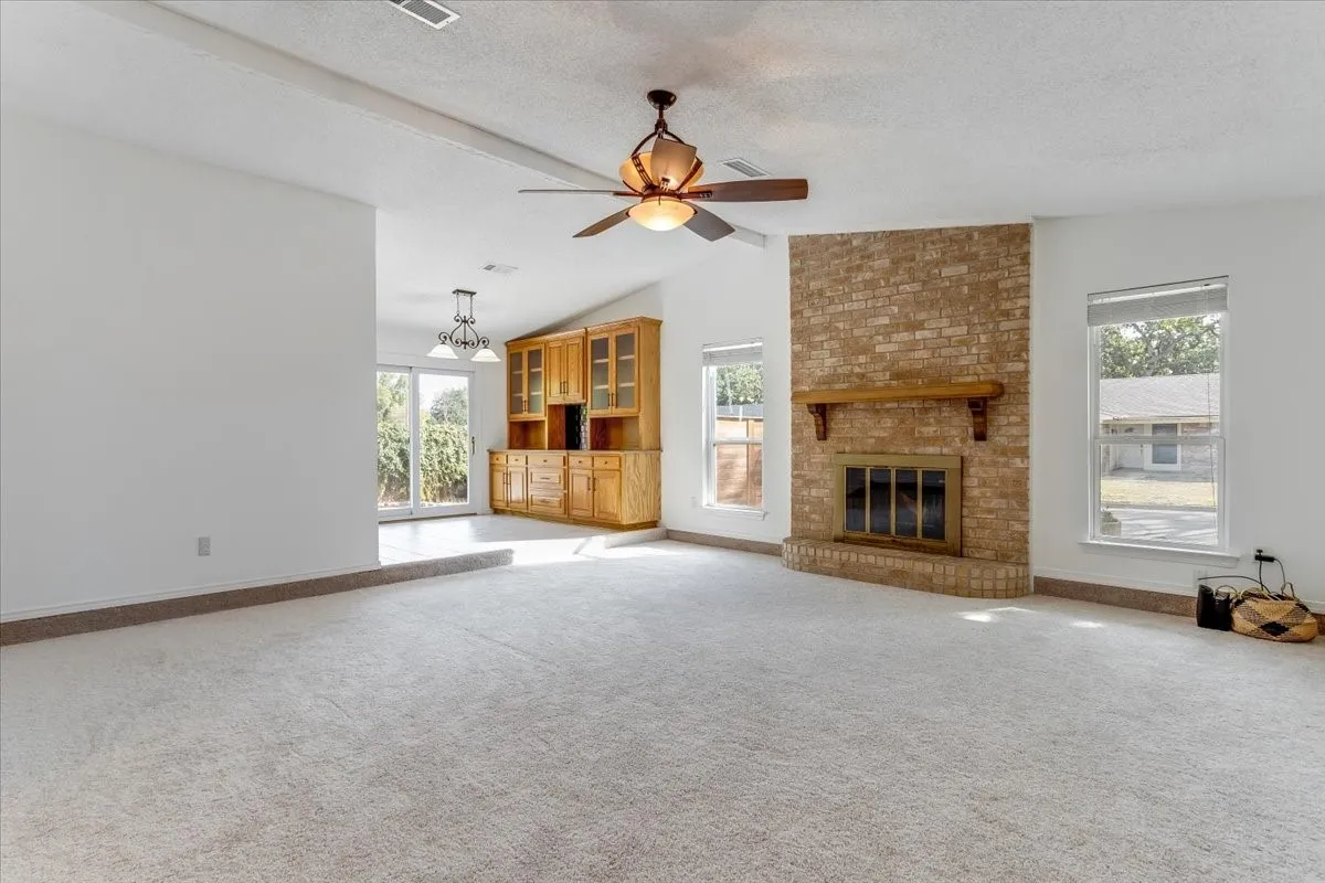 Vaulted ceilings with a ceiling fan, brick fireplace with wood mantel, built-in wooden cabinetry, and sliding glass doors