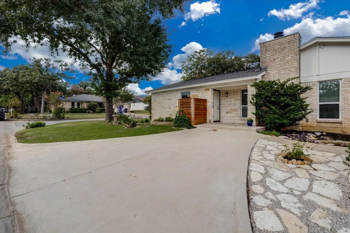 Stone veneer exterior with a concrete driveway, mature landscaping, and a flagstone pathway