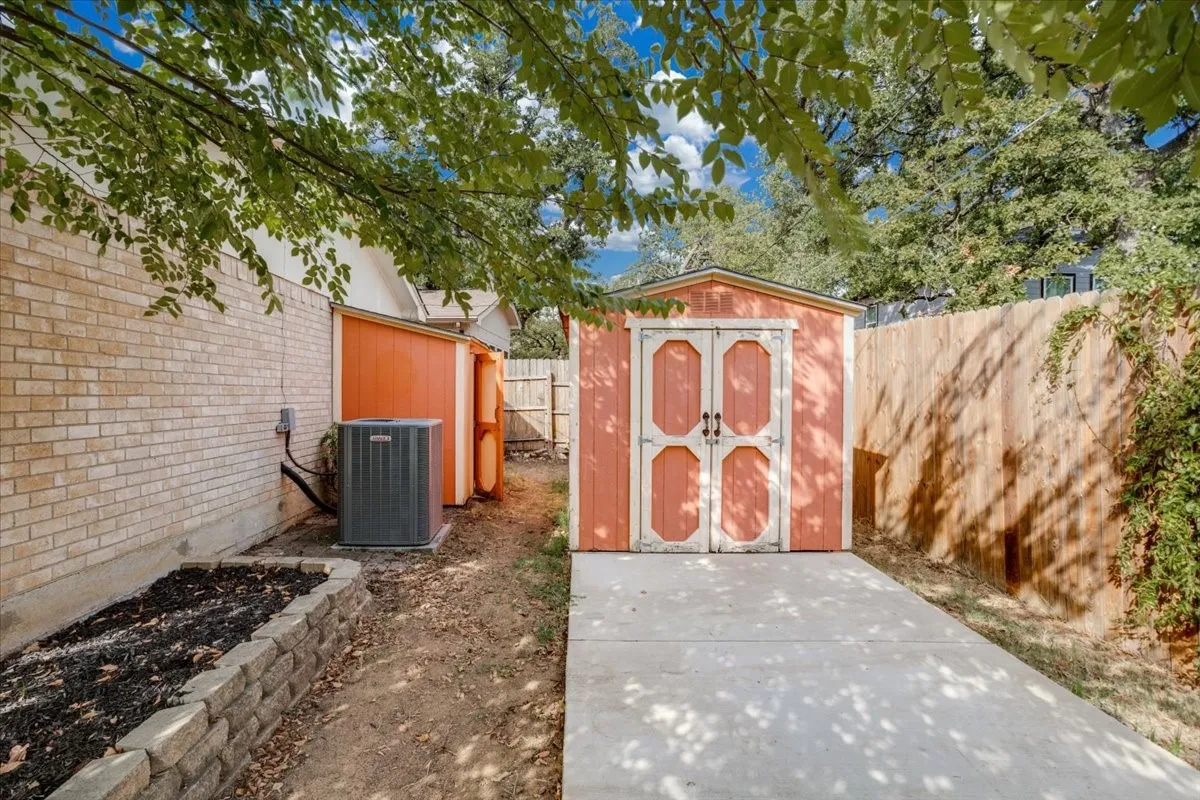 Brick exterior with a storage shed featuring double doors, an additional shed, a wooden privacy fence, and a concrete pathway