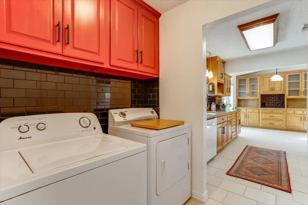 Red-finished upper cabinetry with dark hardware, black subway tile backsplash, and light-toned tile flooring