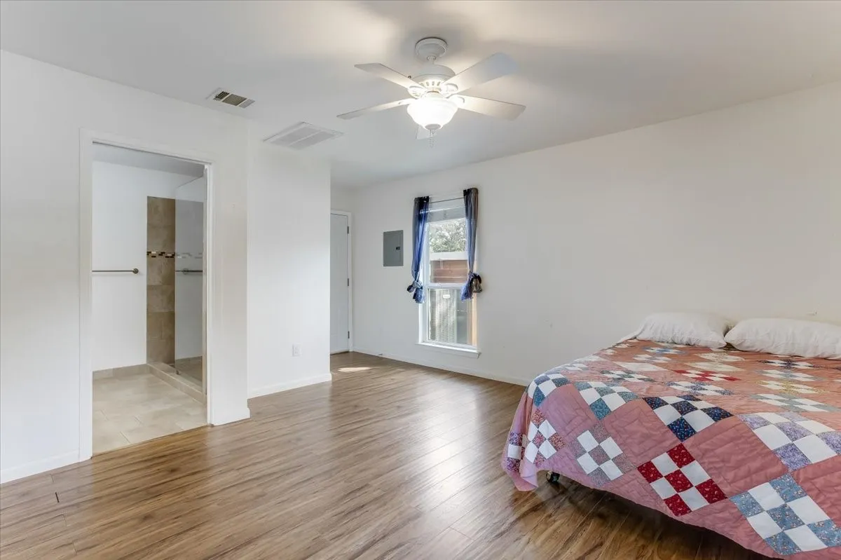 Room featuring wood-finish flooring, a ceiling fan with integrated lighting, and a window with dark-colored curtains