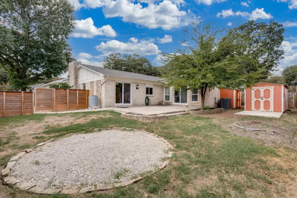 Expansive backyard featuring a stone patio, privacy fencing, two storage sheds, and a gravel-filled circular hardscape