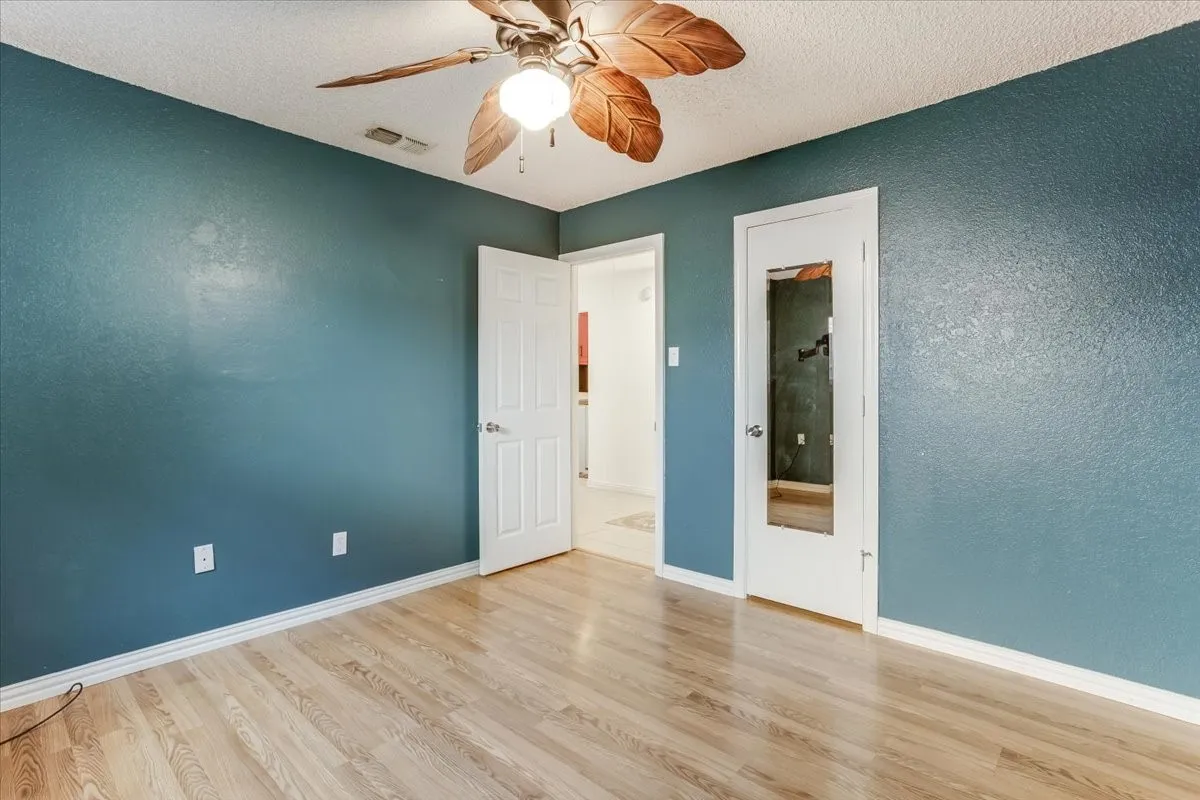 Wood-finish flooring, textured blue walls, white trim, and a ceiling fan with integrated lighting