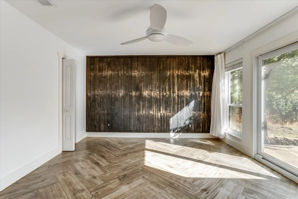 Herringbone wood-finish flooring, accent wall with distressed wood paneling, contemporary ceiling fan, and large windows