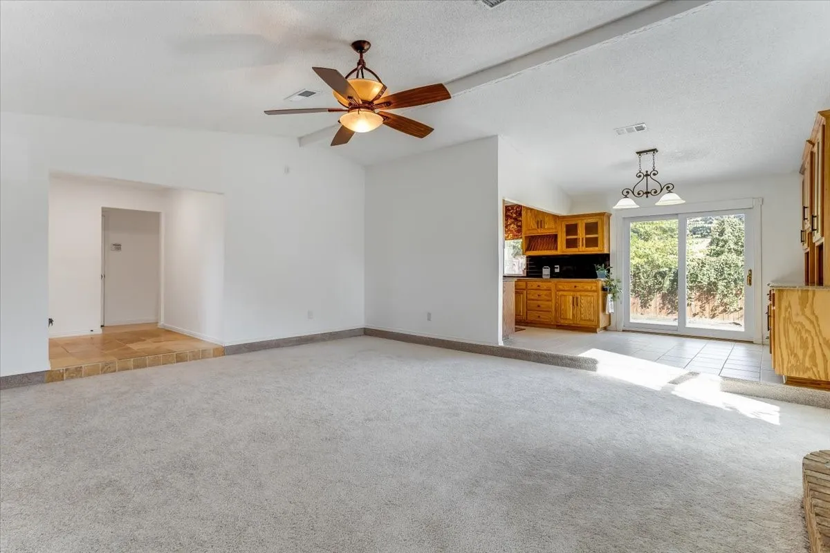 Vaulted ceiling with a ceiling fan, carpeted flooring, tiled flooring, wooden cabinetry, and sliding glass doors