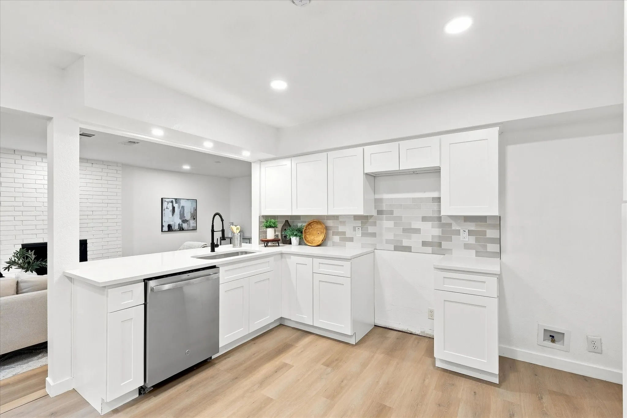 Modern kitchen featuring white cabinetry, light countertops, wood-finish flooring, a stainless steel dishwasher, and a tile backsplash