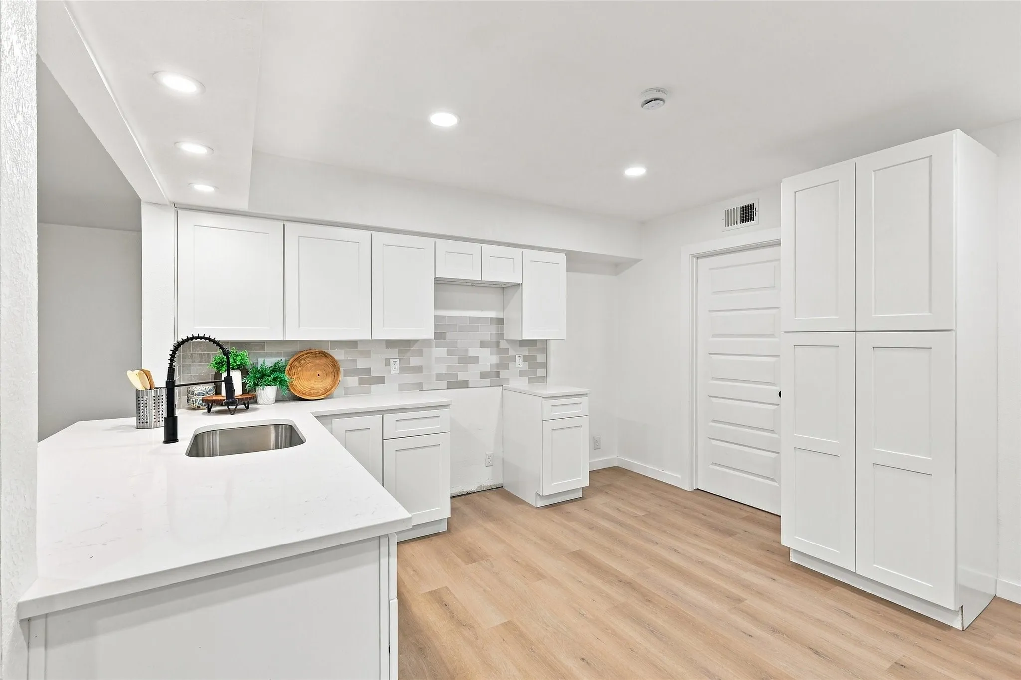 White cabinetry, light-toned wood-finish flooring, recessed lighting, white countertops, and a stainless steel sink with a matte black faucet