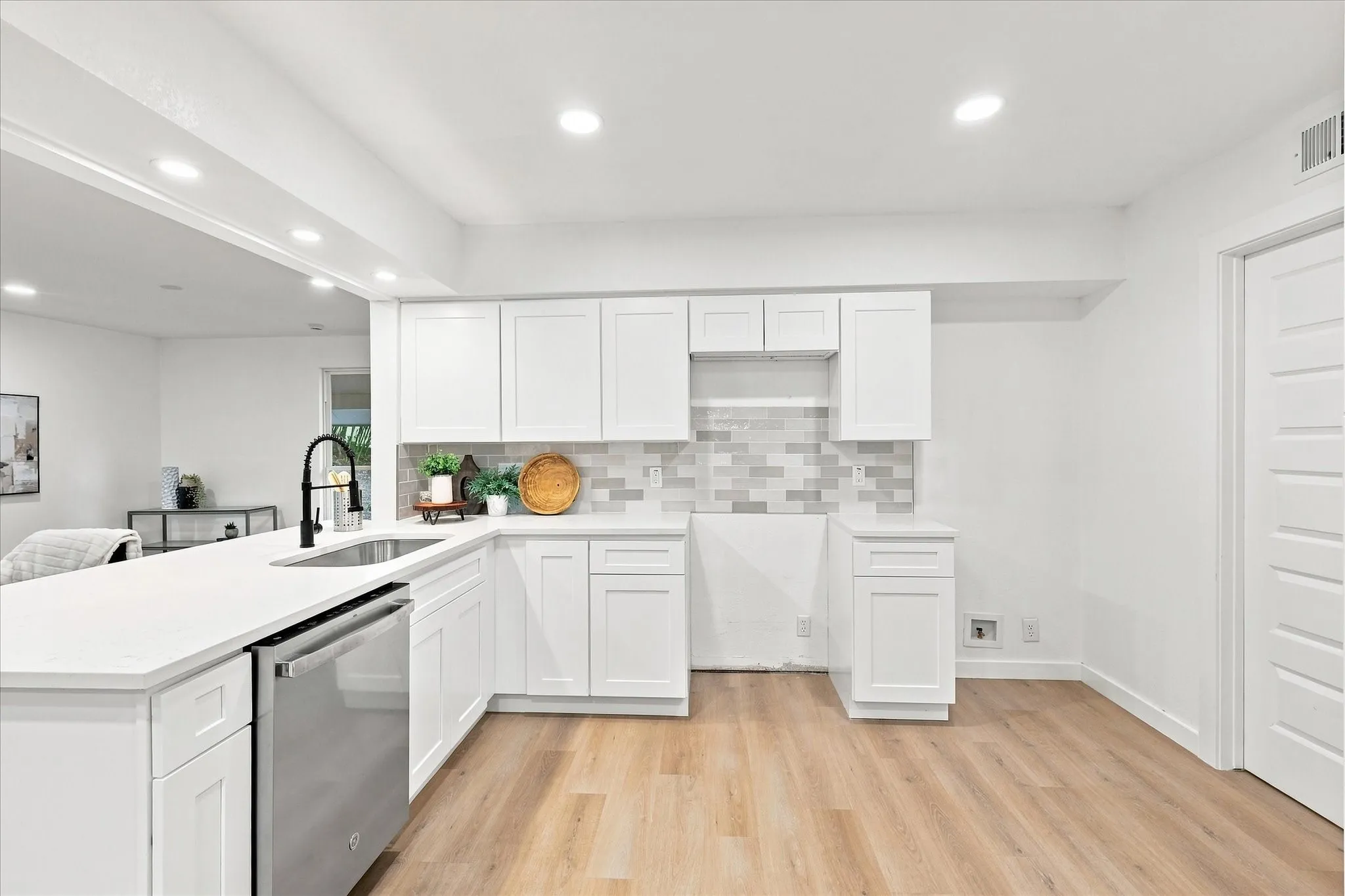 Modern kitchen featuring white shaker cabinetry, stainless steel dishwasher, white countertops, a mosaic tile backsplash, and light wood-finish flooring