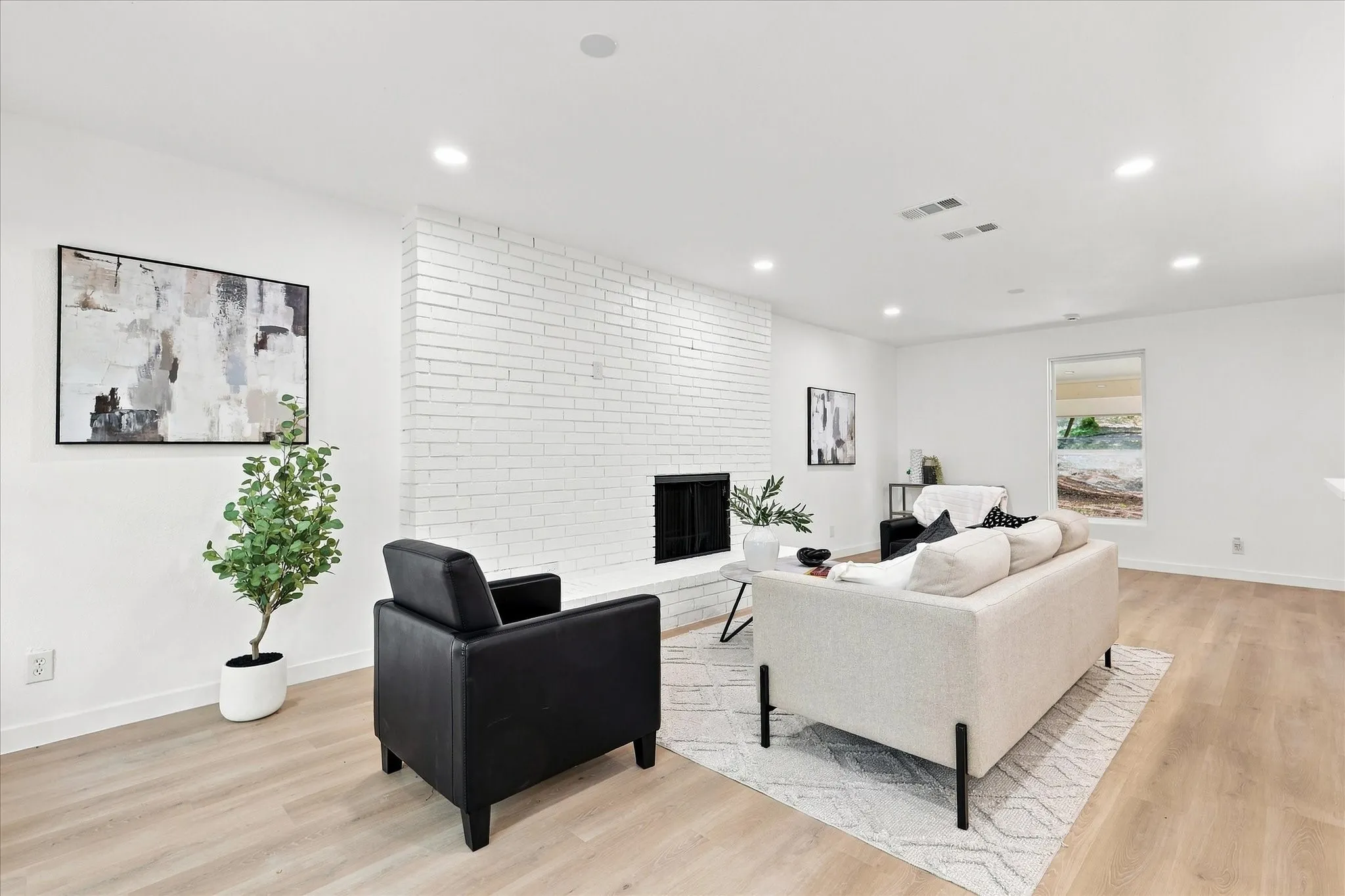 Open-concept living space featuring a white brick fireplace, recessed lighting, and wood-finish flooring
