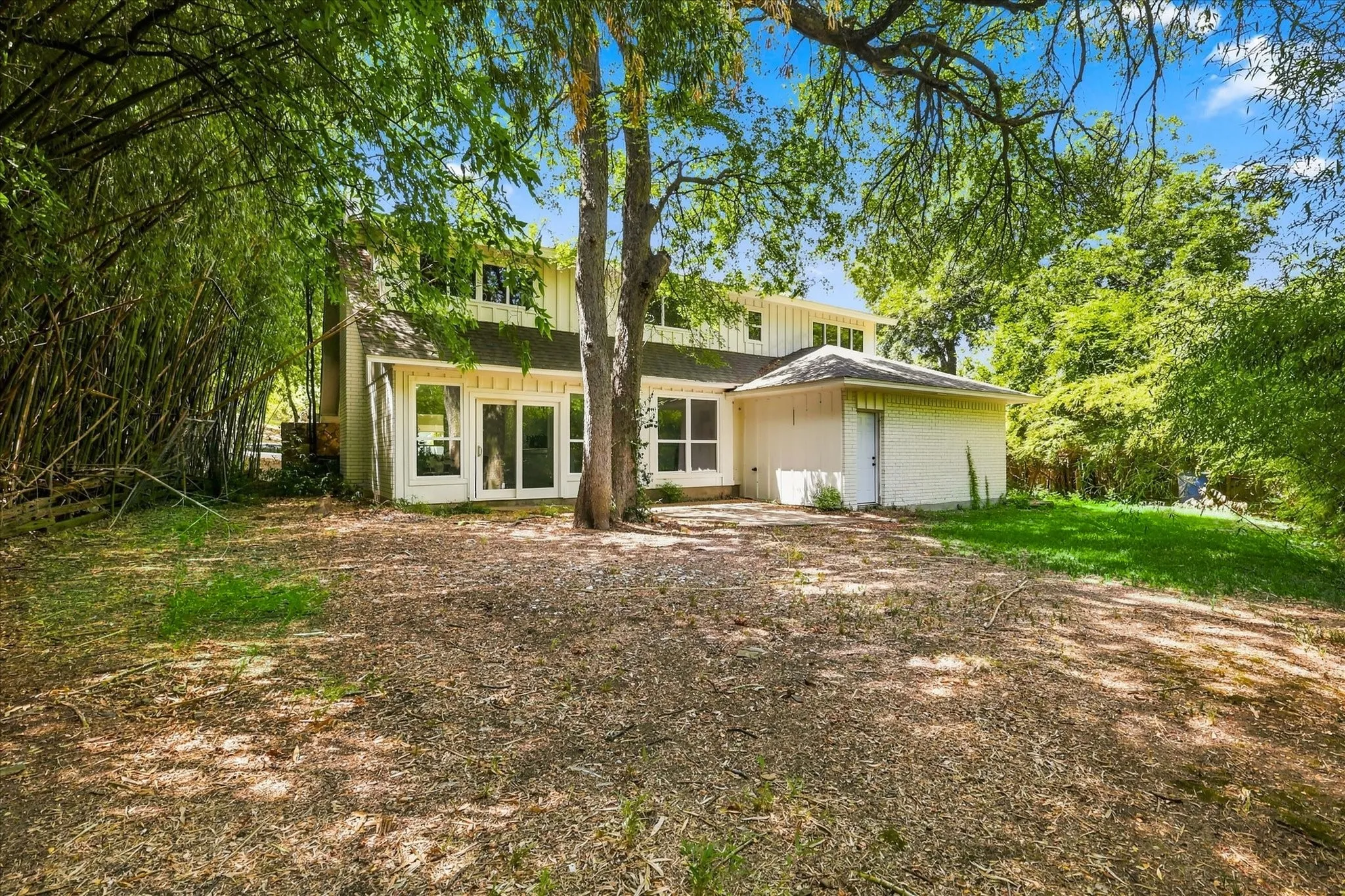 Expansive backyard featuring mature trees, a ground-level patio, and sliding glass doors