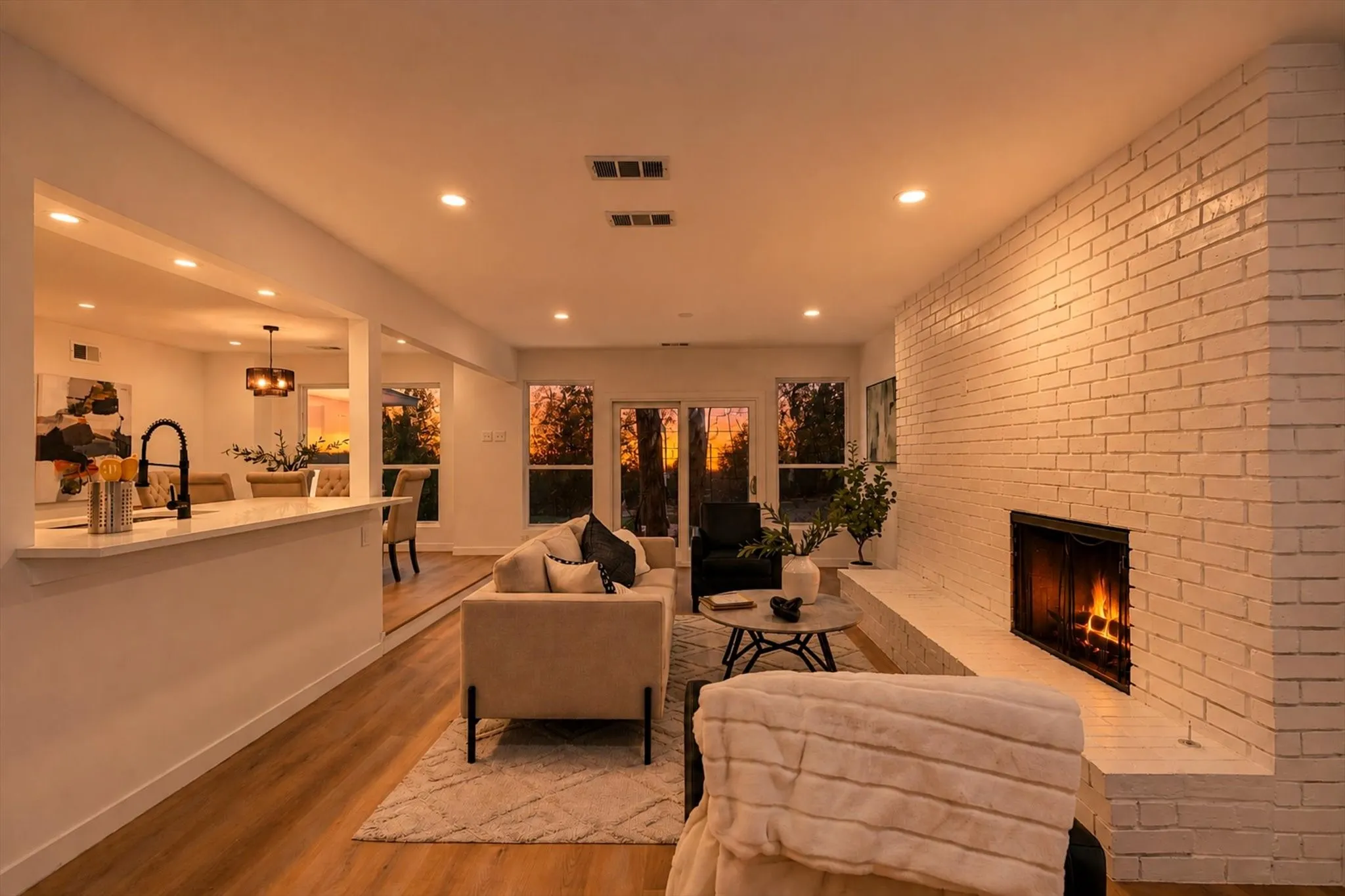 Expansive living area featuring wood-finish flooring, a white brick fireplace, recessed lighting, and sliding glass doors