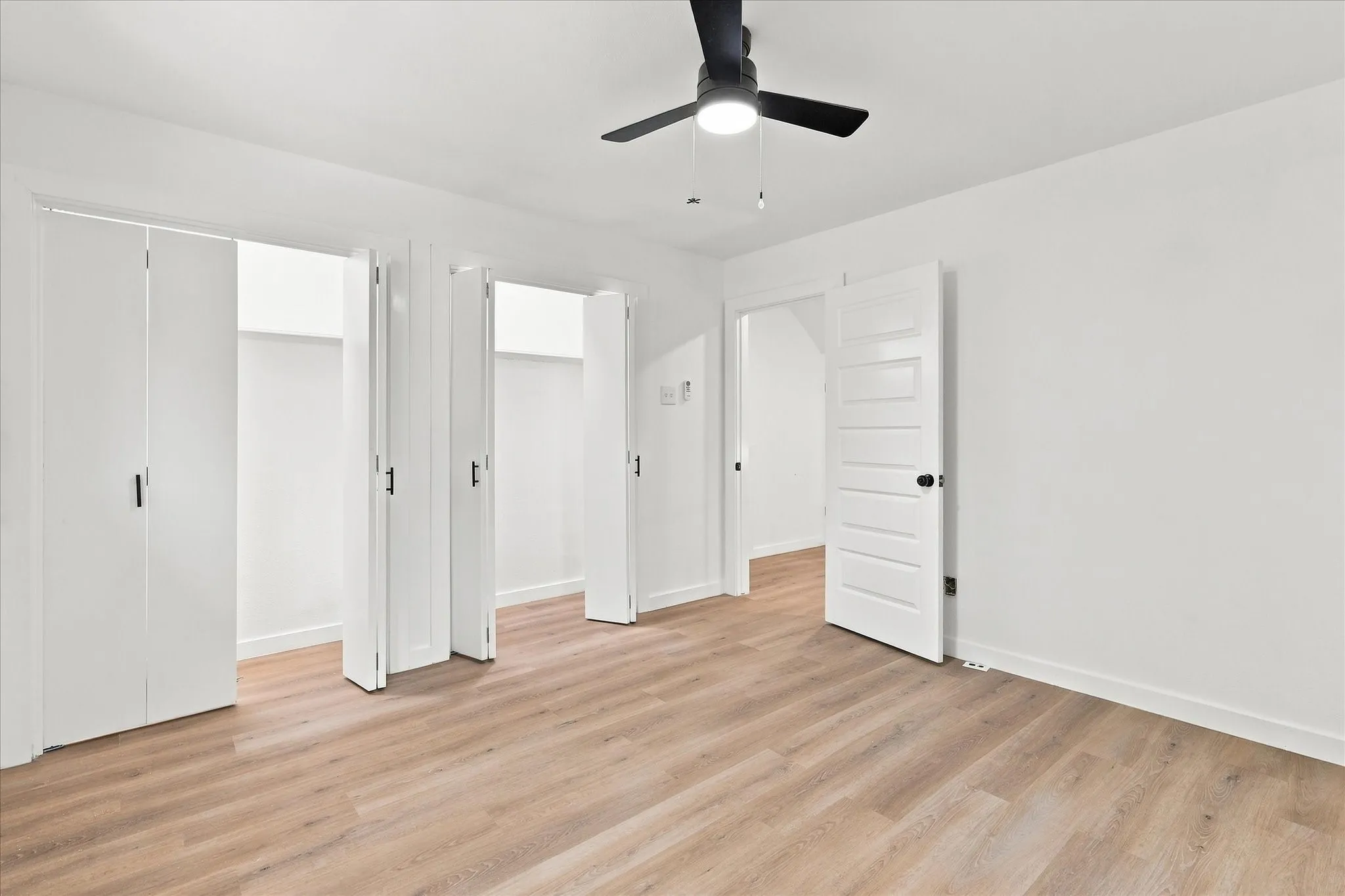 Recessed lighting, wood-finish flooring, white walls, black ceiling fan, and white paneled doors