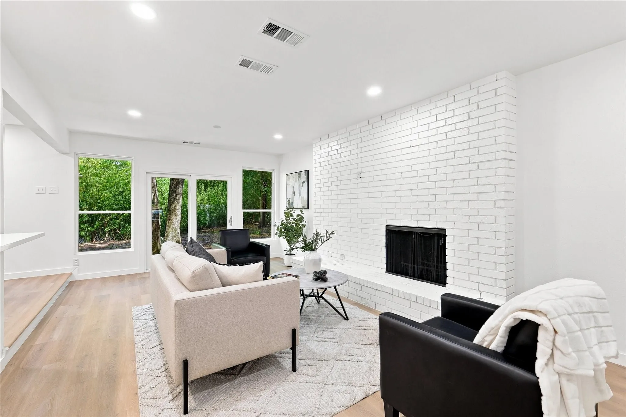 Painted brick fireplace with hearth, recessed lighting, wood-finish flooring, and multiple large windows
