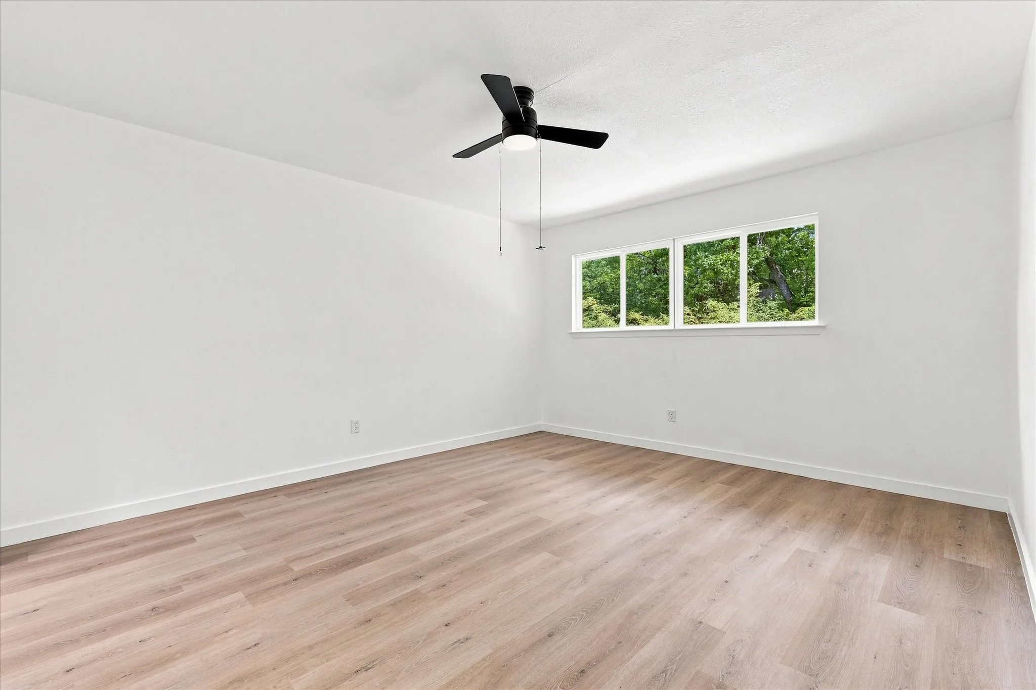 Neutral wall finishes, wood-finish flooring, multiple windows, black ceiling fan