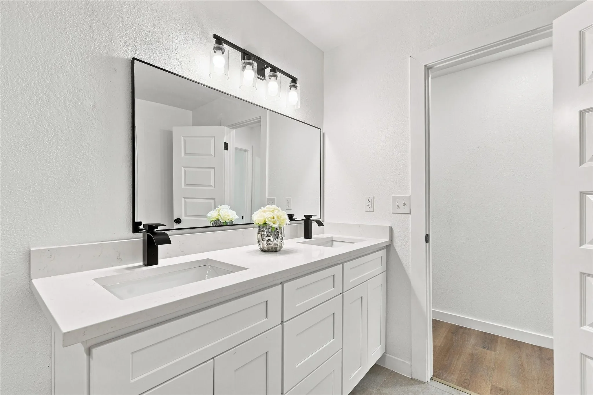 Dual white rectangular undermount sinks, white countertop, white shaker-style cabinetry, matte black faucets, and a black-framed rectangular mirror