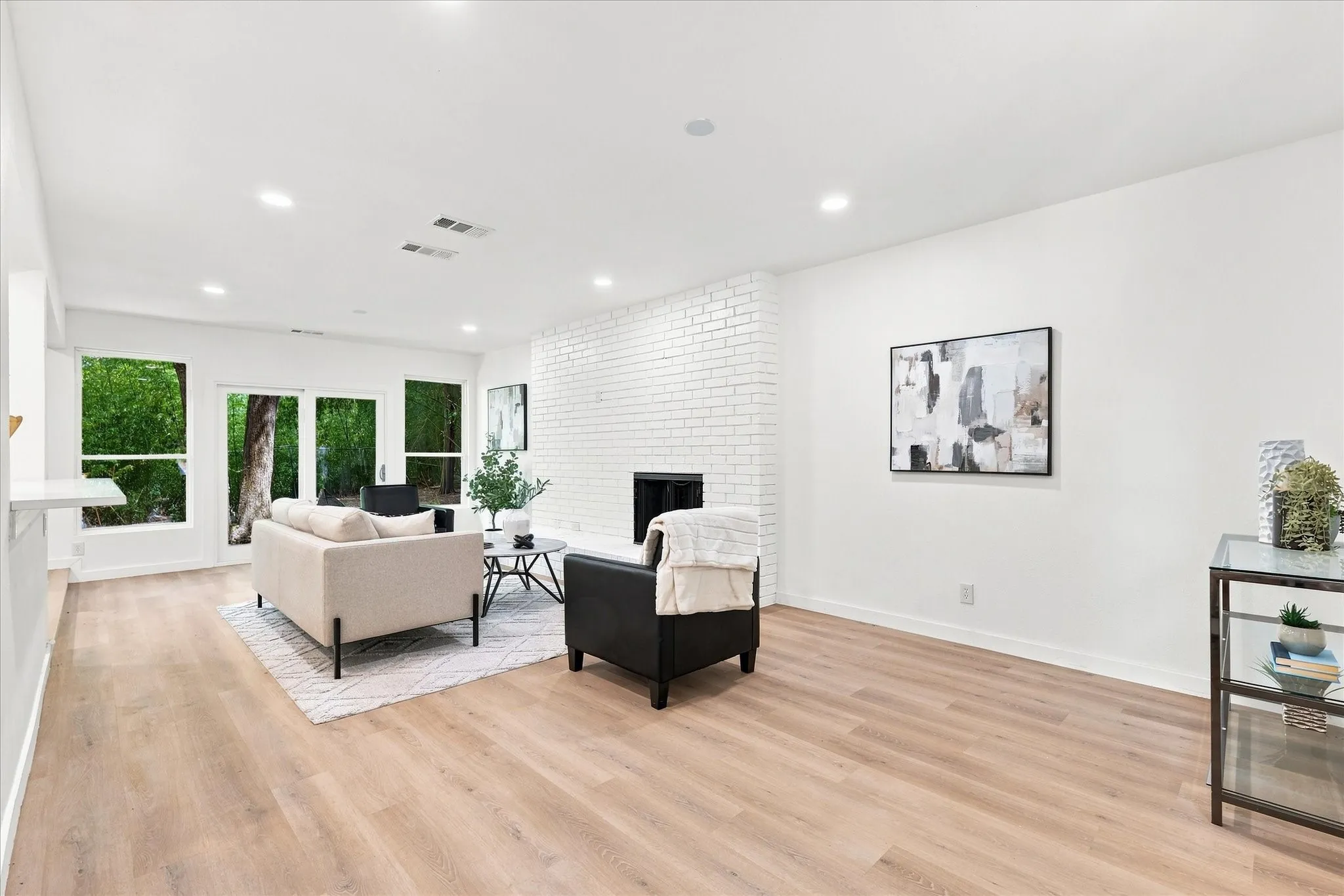 Wood-finish flooring throughout, white painted brick fireplace, recessed lighting, and multiple windows