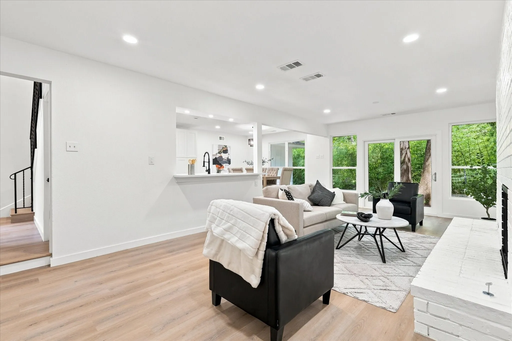 Recessed lighting throughout, wood-finish flooring, white brick fireplace, sliding glass door, and an open pass-through to the kitchen