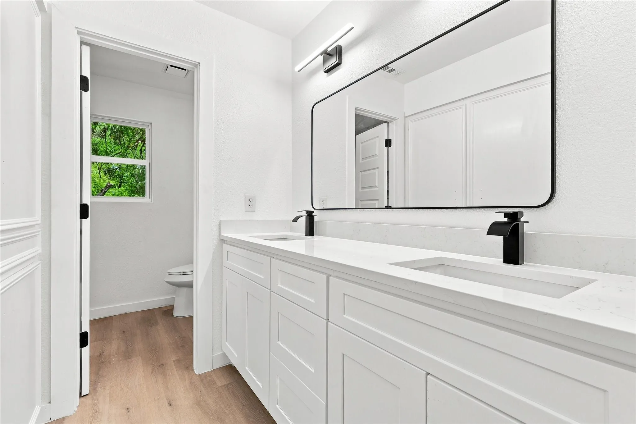 Dual vanity with integrated rectangular sinks, white cabinetry, matte black faucets, white countertops, and a large black-framed mirror