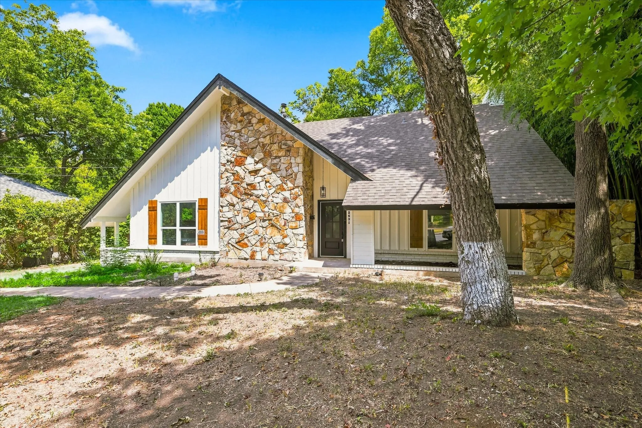 Gable roofline featuring vertical siding, stone veneer accents, wood window shutters, a front entry door, and a covered porch