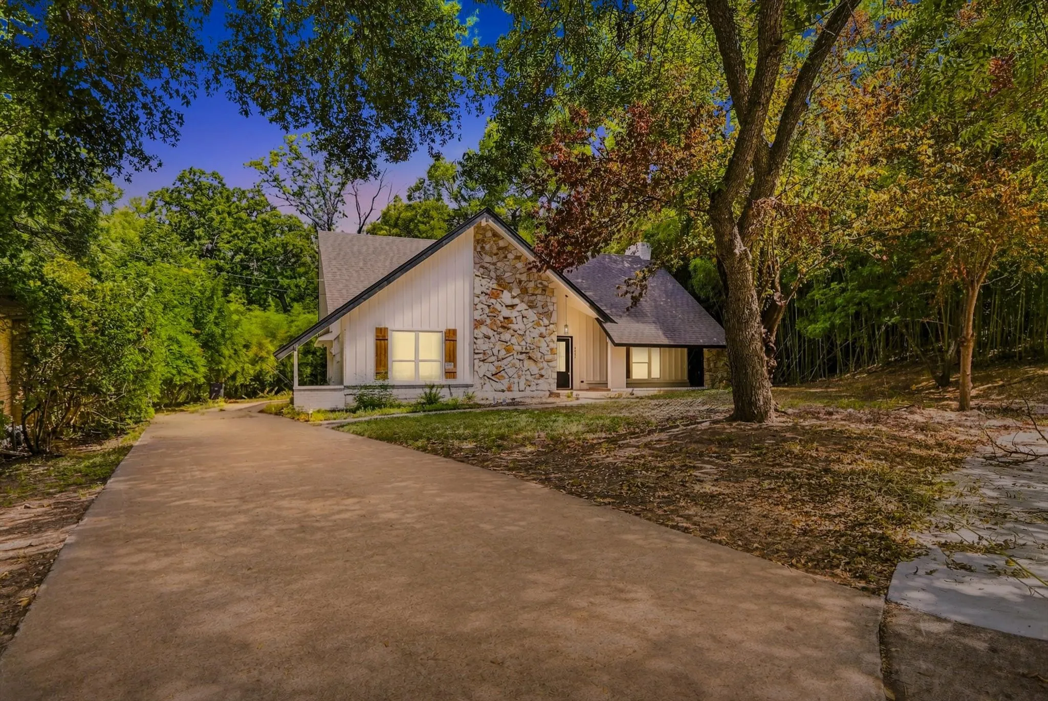 White vertical siding exterior with natural stone accents and a dark shingle roof