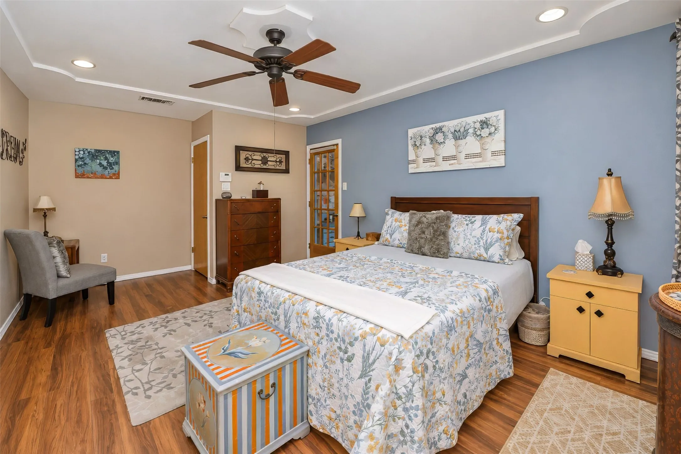 Wood-finish flooring throughout, tray ceiling with recessed lighting and a ceiling fan, and a wood-paneled door