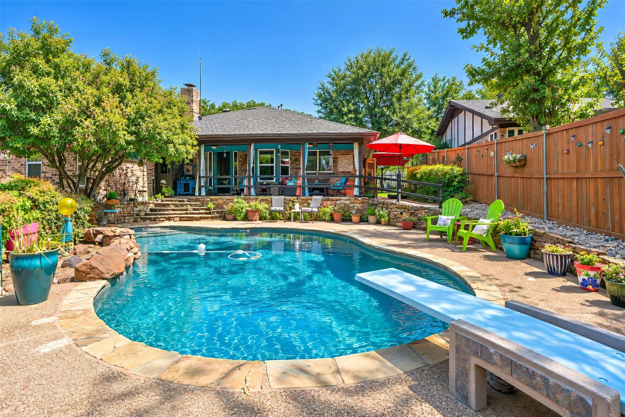 Curved swimming pool with an integrated diving board, surrounded by stone coping and a flagstone patio