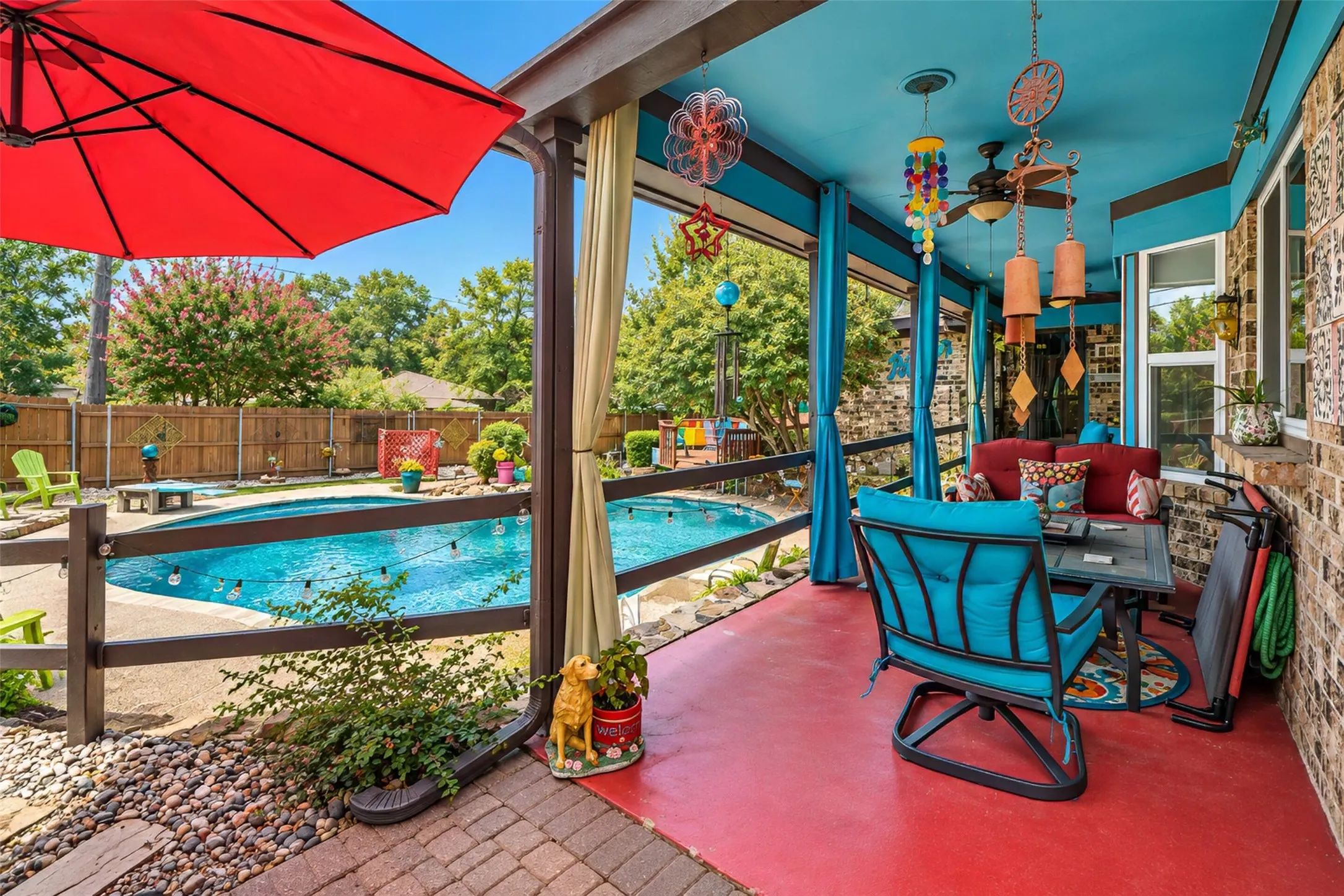 Covered outdoor patio with a vibrant blue ceiling and red concrete flooring, featuring a ceiling fan and integrated lighting