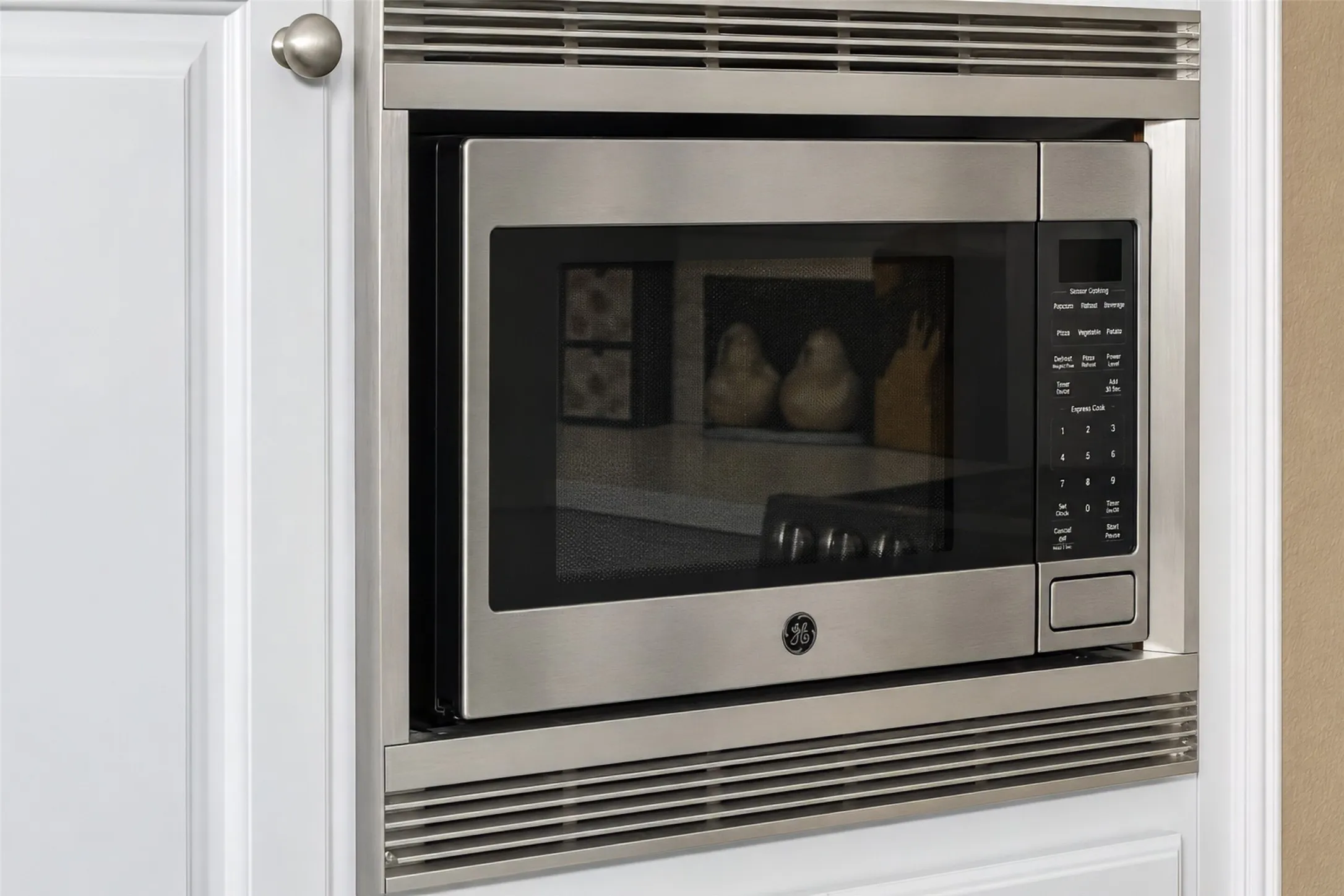 Stainless steel built-in microwave oven, integrated into white panel cabinetry with brushed nickel hardware