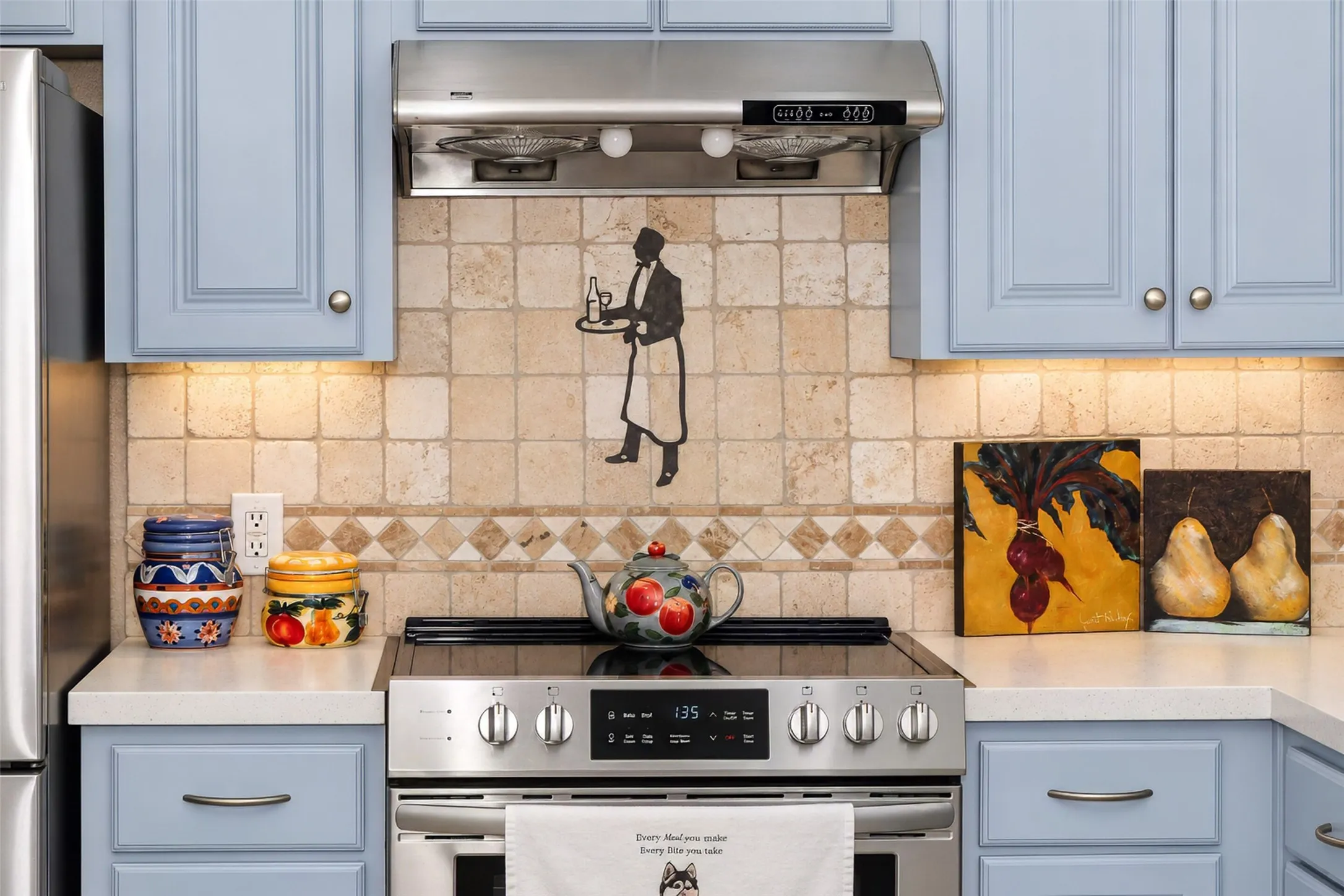 Stainless steel electric range with a coordinating range hood, stone tile backsplash, light-toned countertops, and light blue cabinetry