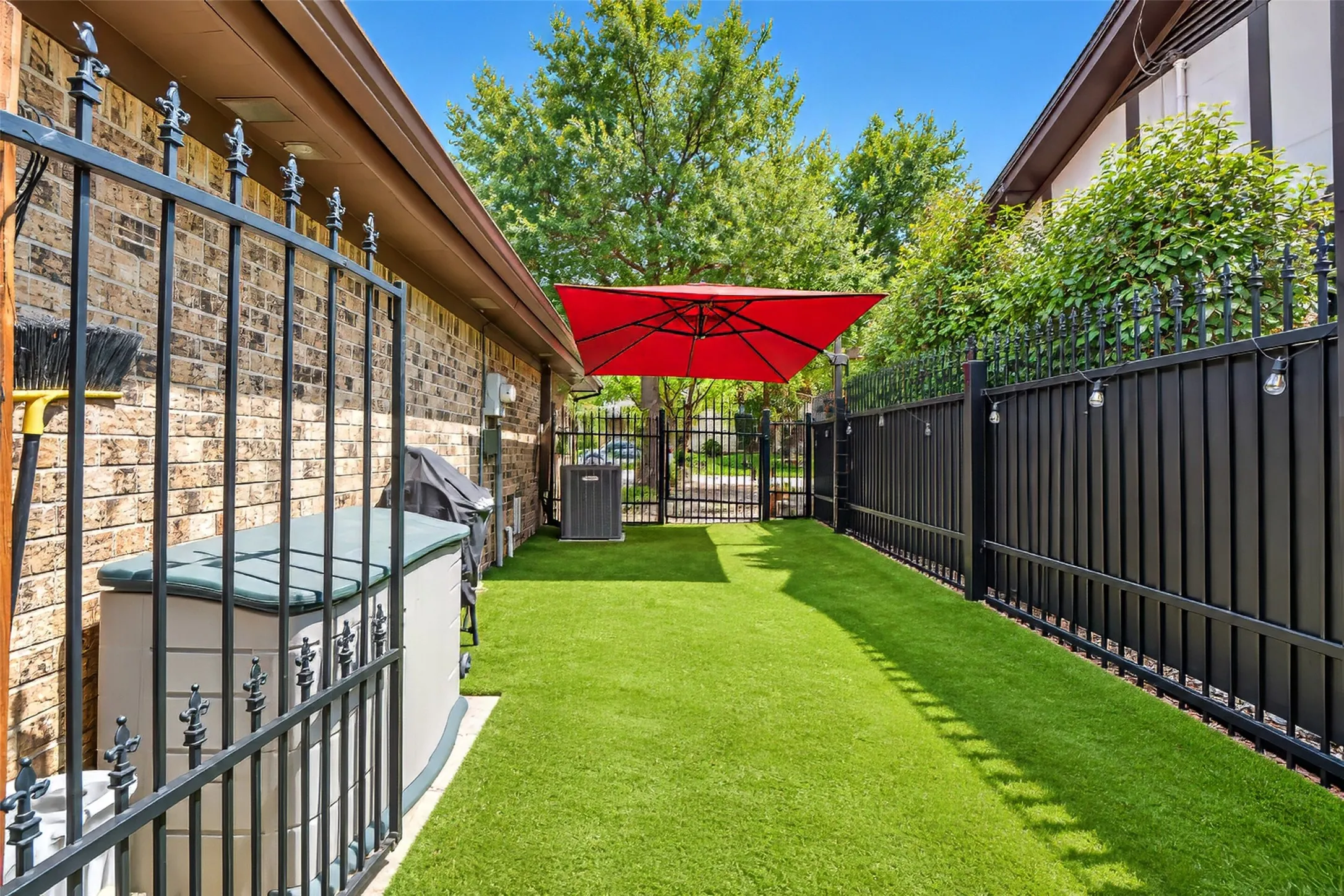 Outdoor space featuring artificial turf, black metal fencing, and brick exterior