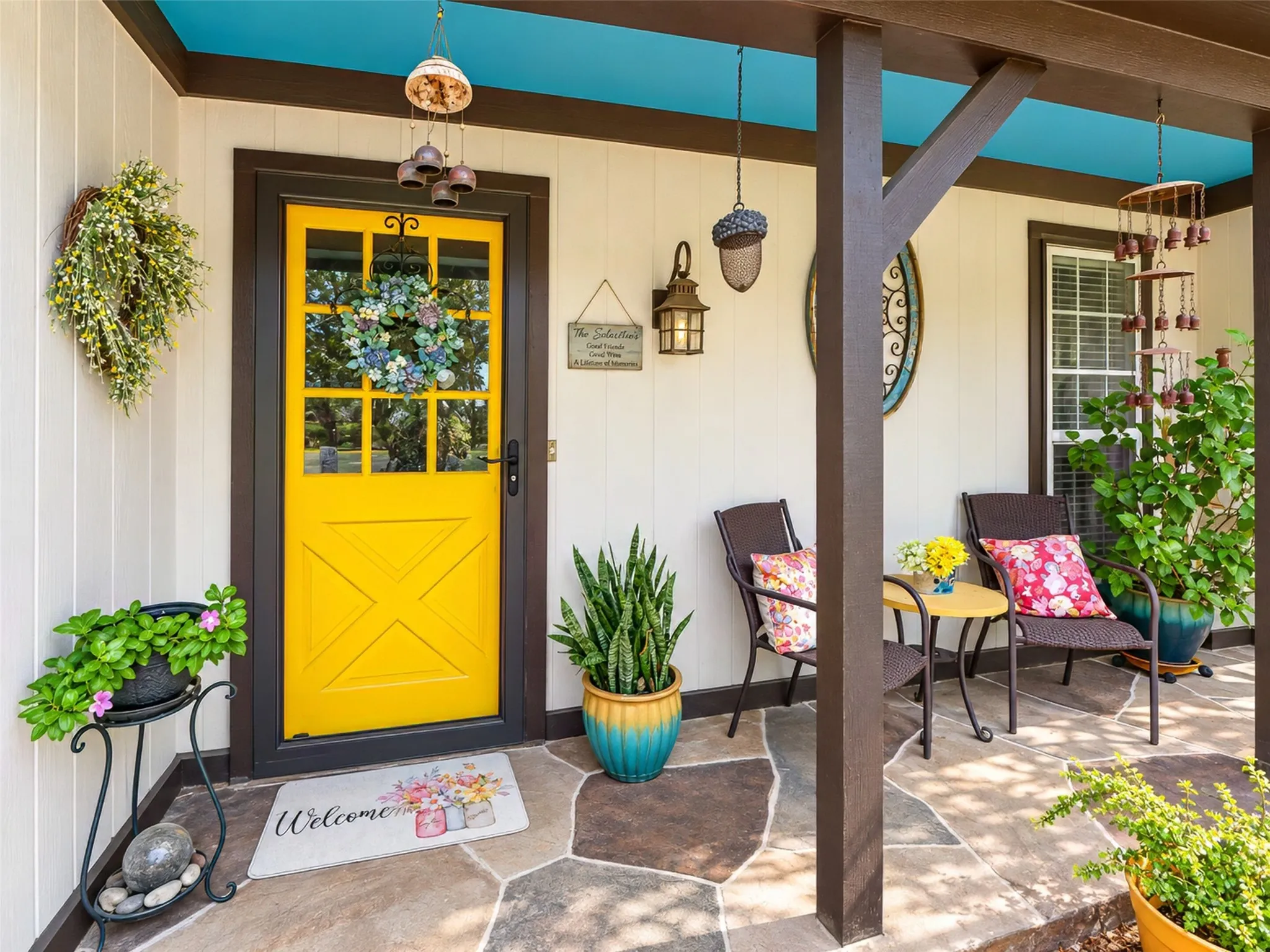 Flagstone porch featuring a bold yellow door with glass panels, painted blue ceiling, and white vertical siding