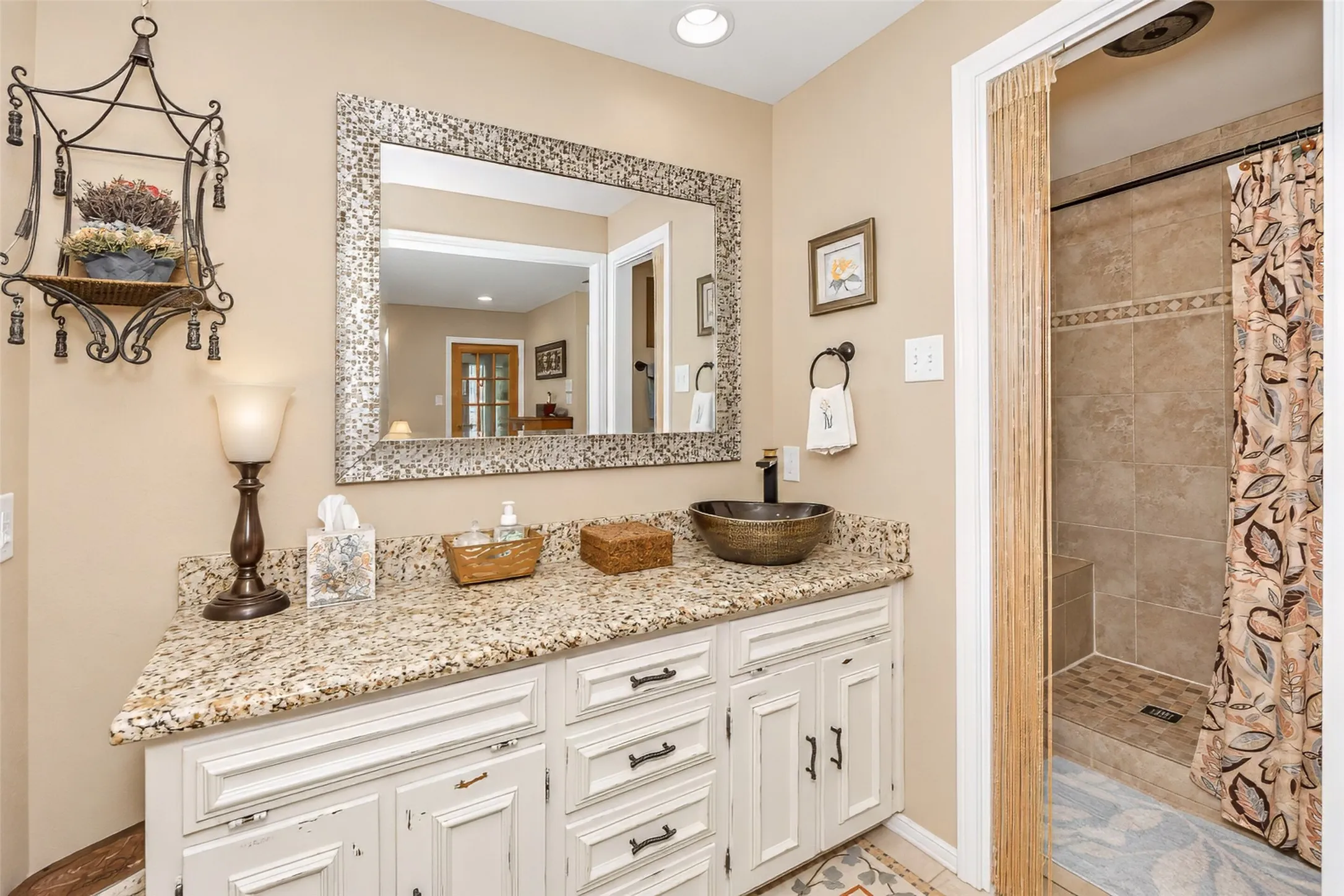 Granite-style countertop with a vessel sink, white vanity cabinetry with dark hardware, and a tiled shower with a rain-style showerhead