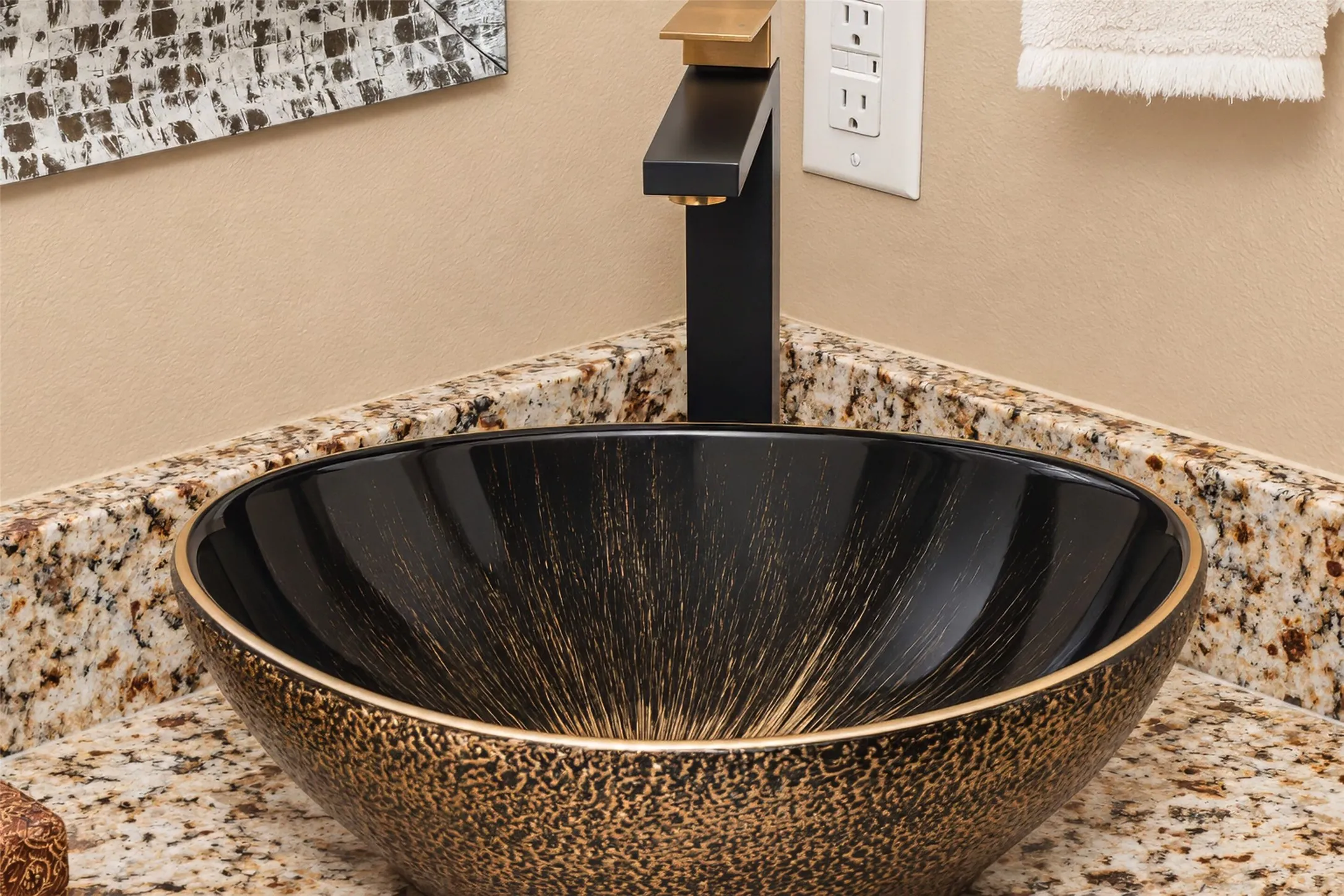 Vessel sink with a textured exterior, black and gold-toned faucet, and granite countertop