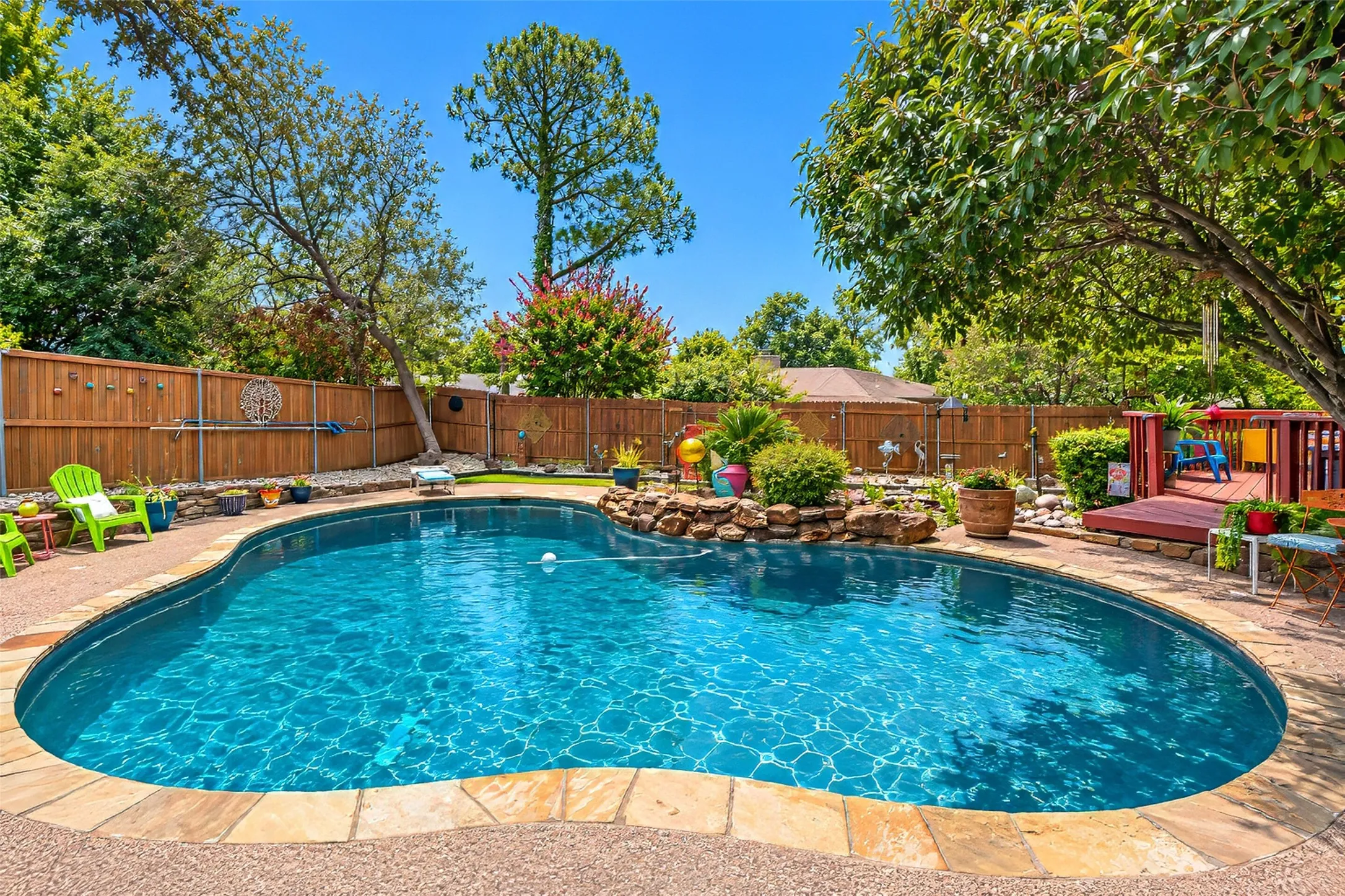 Freeform swimming pool with rock wall, flagstone coping, and a wooden privacy fence
